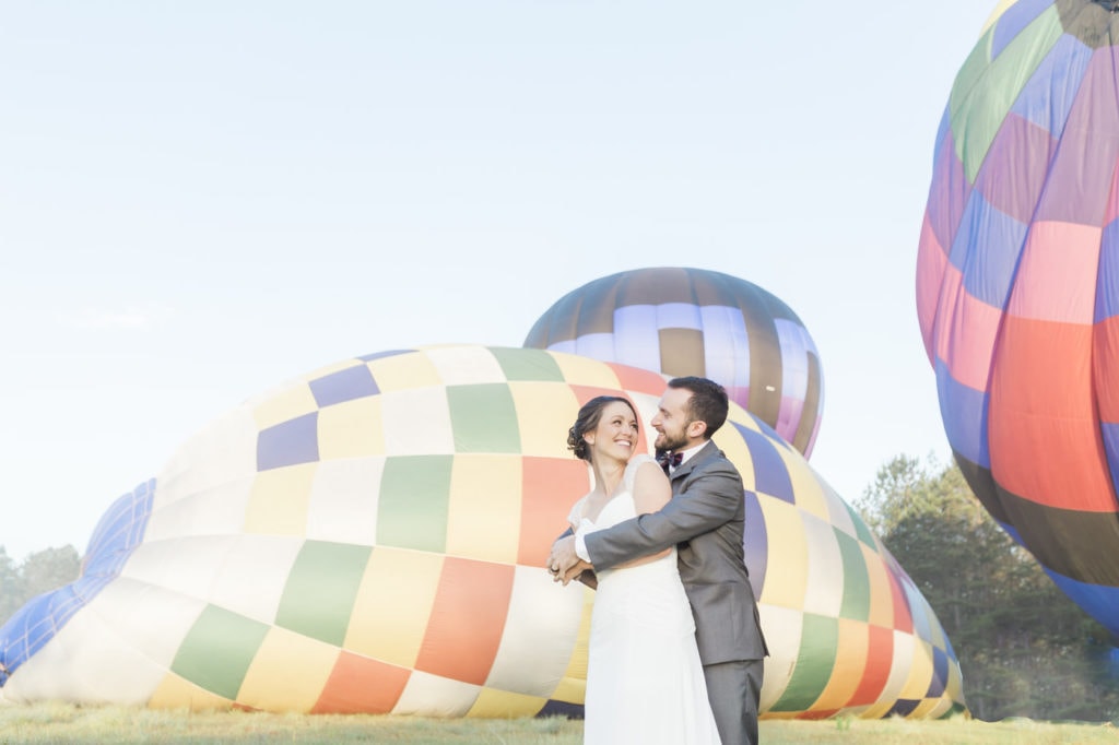 bride and groom laughing with hot air balloons inflating in the background