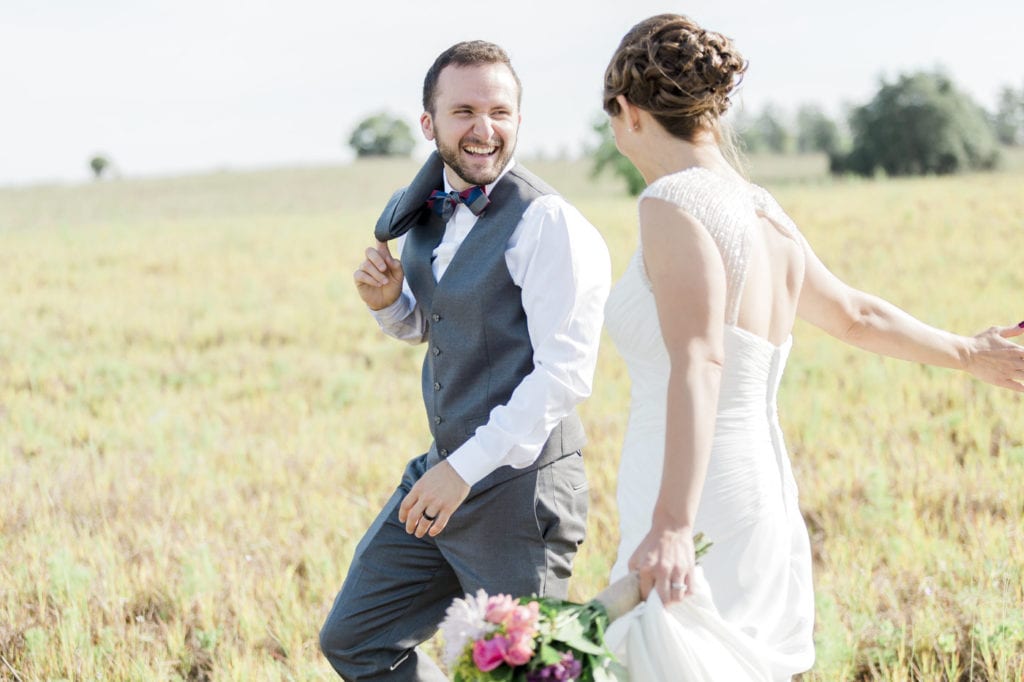 groom laughing while walking with bride in big field
