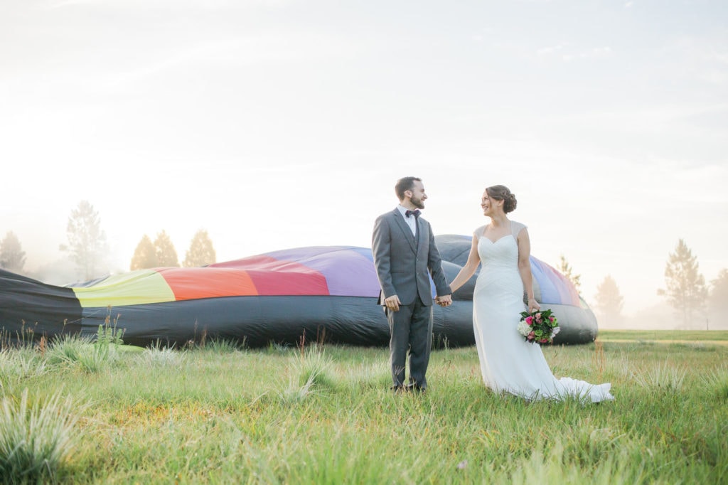 bride and groom holding hands during sunrise with hot air balloon inflating in the background