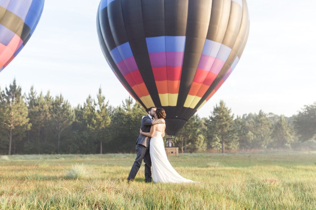 bride and groom kissing in front of painted horizons hot air balloons