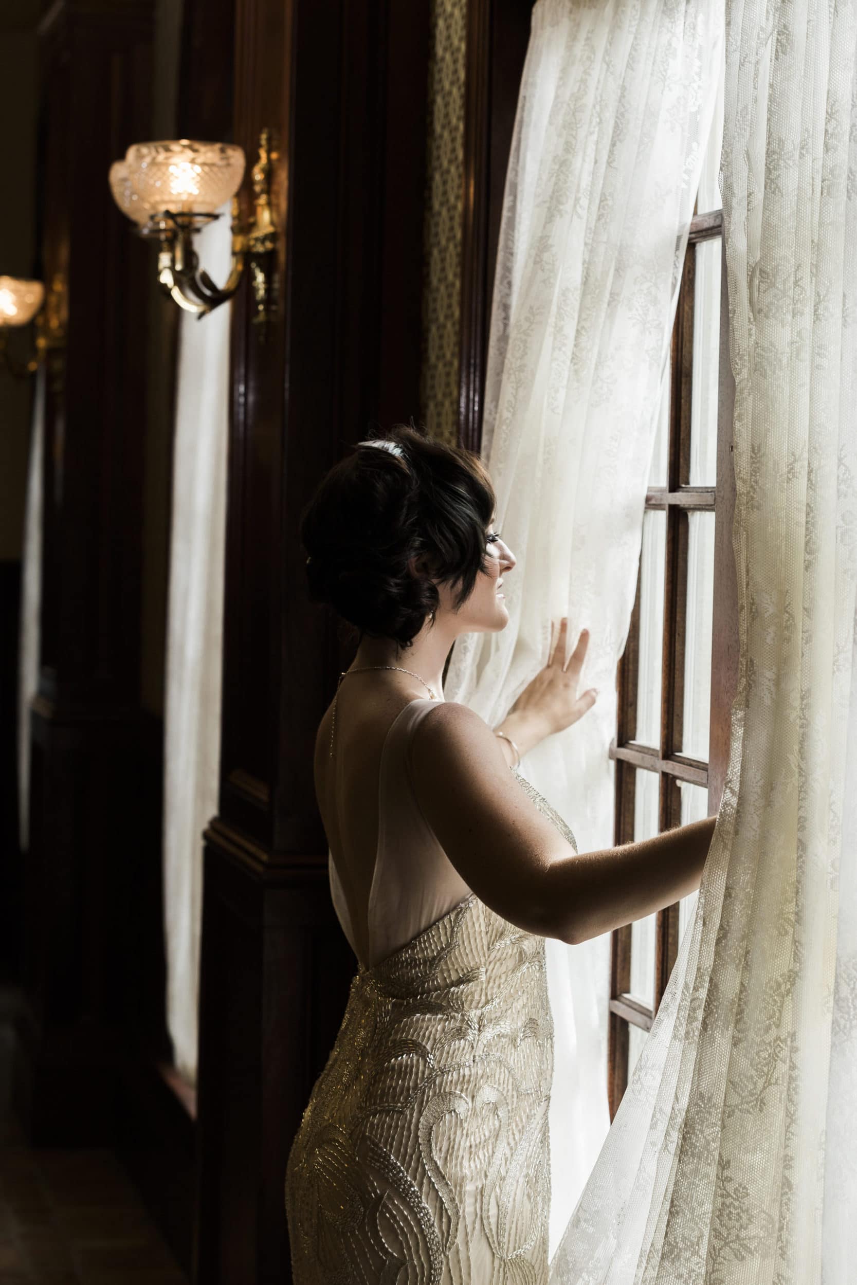 bride with white dress looking out window with white curtains at Star Wars Wedding