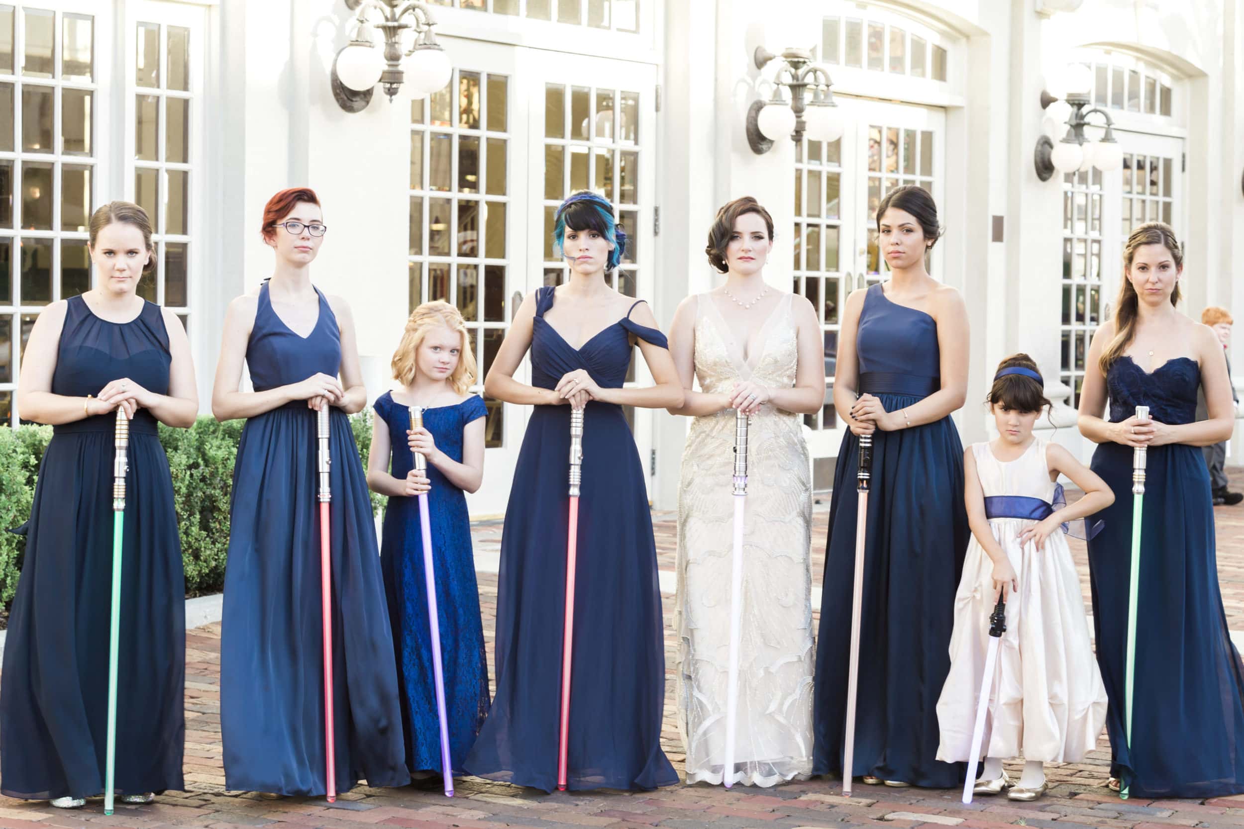 bride with bridesmaids with blue dresses with light sabers with white building in background at Star Wars Wedding