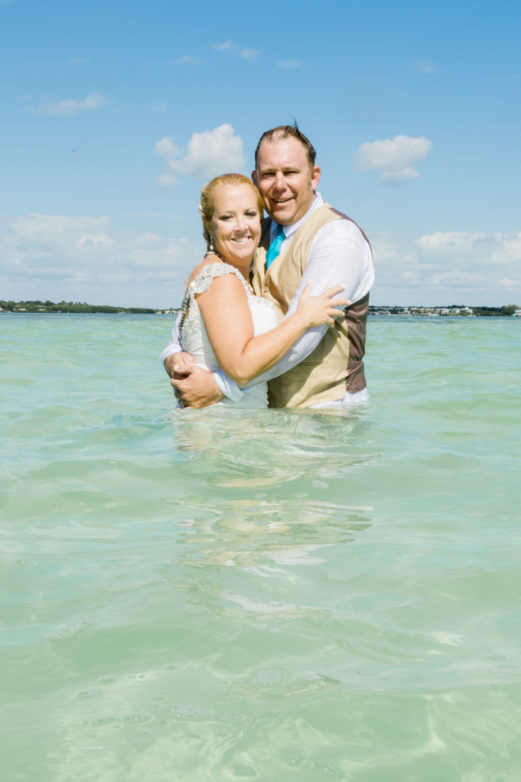 bride with white wet gown with groom with tan suit with teal tie in ocean water at Coconut Cove Resort Wedding