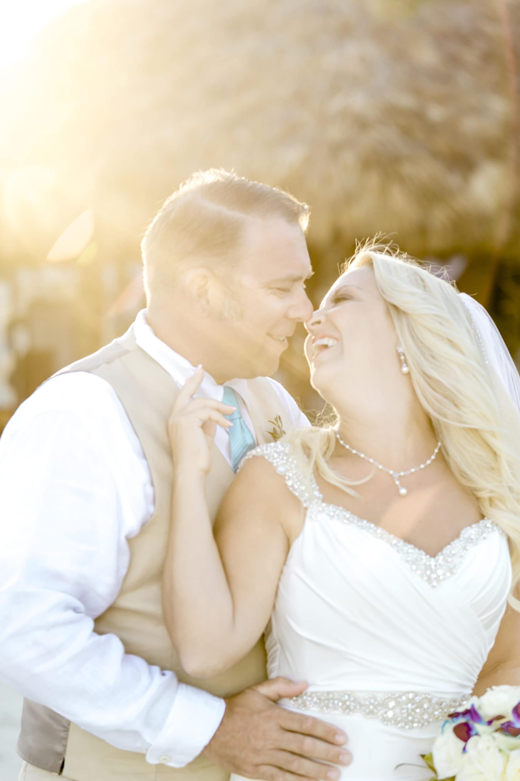 bride with white dress with necklace with groom with tan vest with teal tie with thatched roof building in background at Coconut Cove Resort Wedding