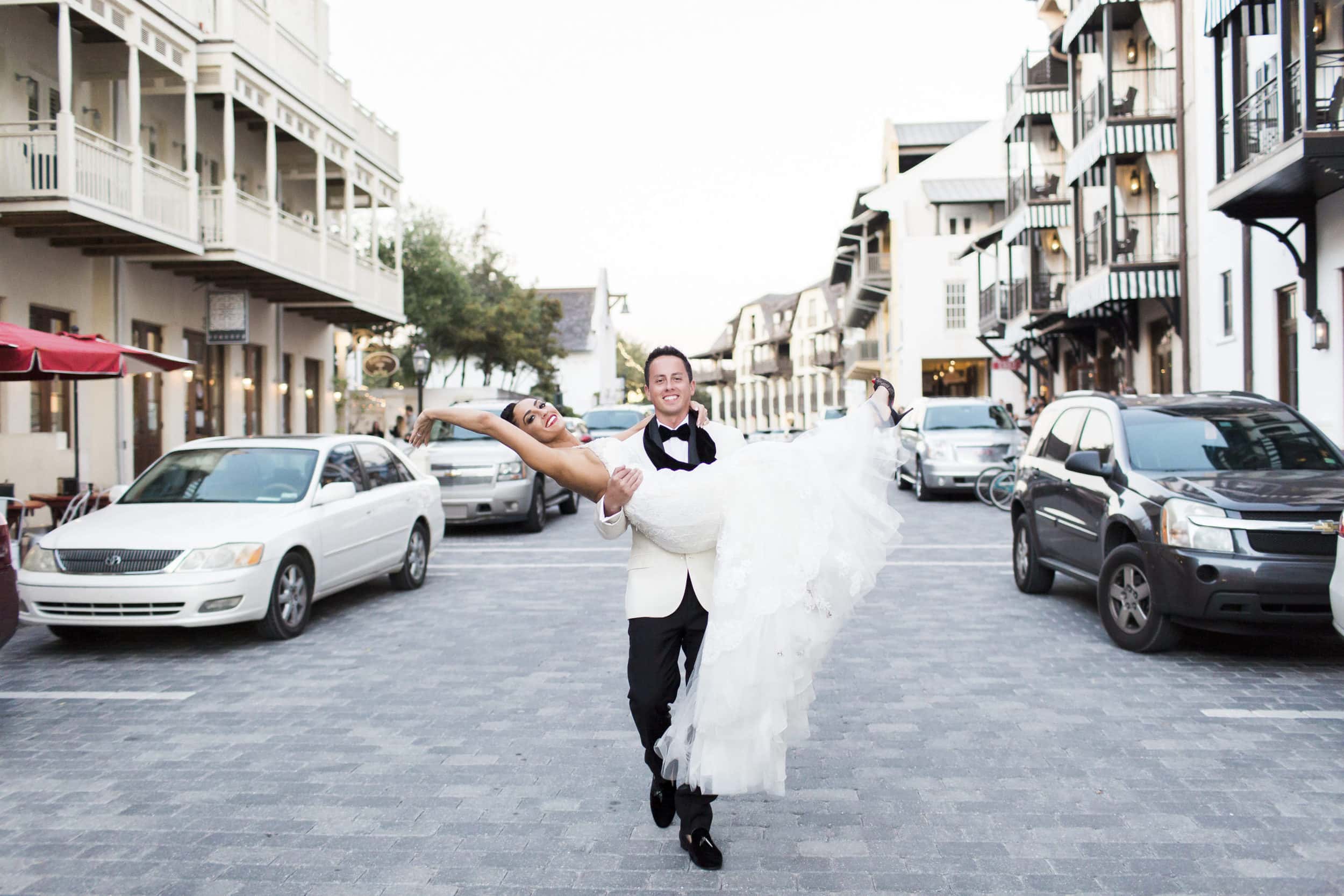 groom carrying bride down the street in his arms in front of the pearl hotel in rosemary beach florida