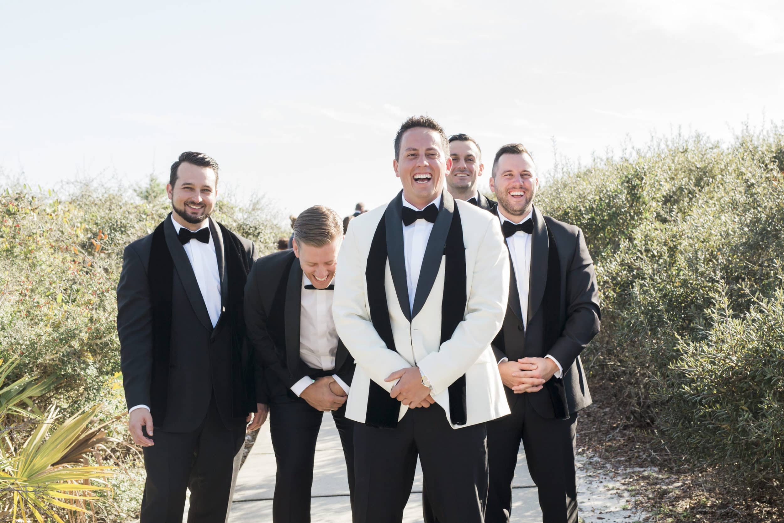 groom and groomsmen laughing while standing on the beach