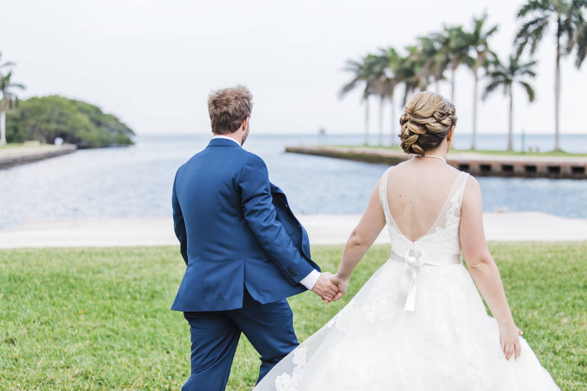 bride in white dress with groom in navy tuxedo with ocean water with palm tress at deering estate wedding