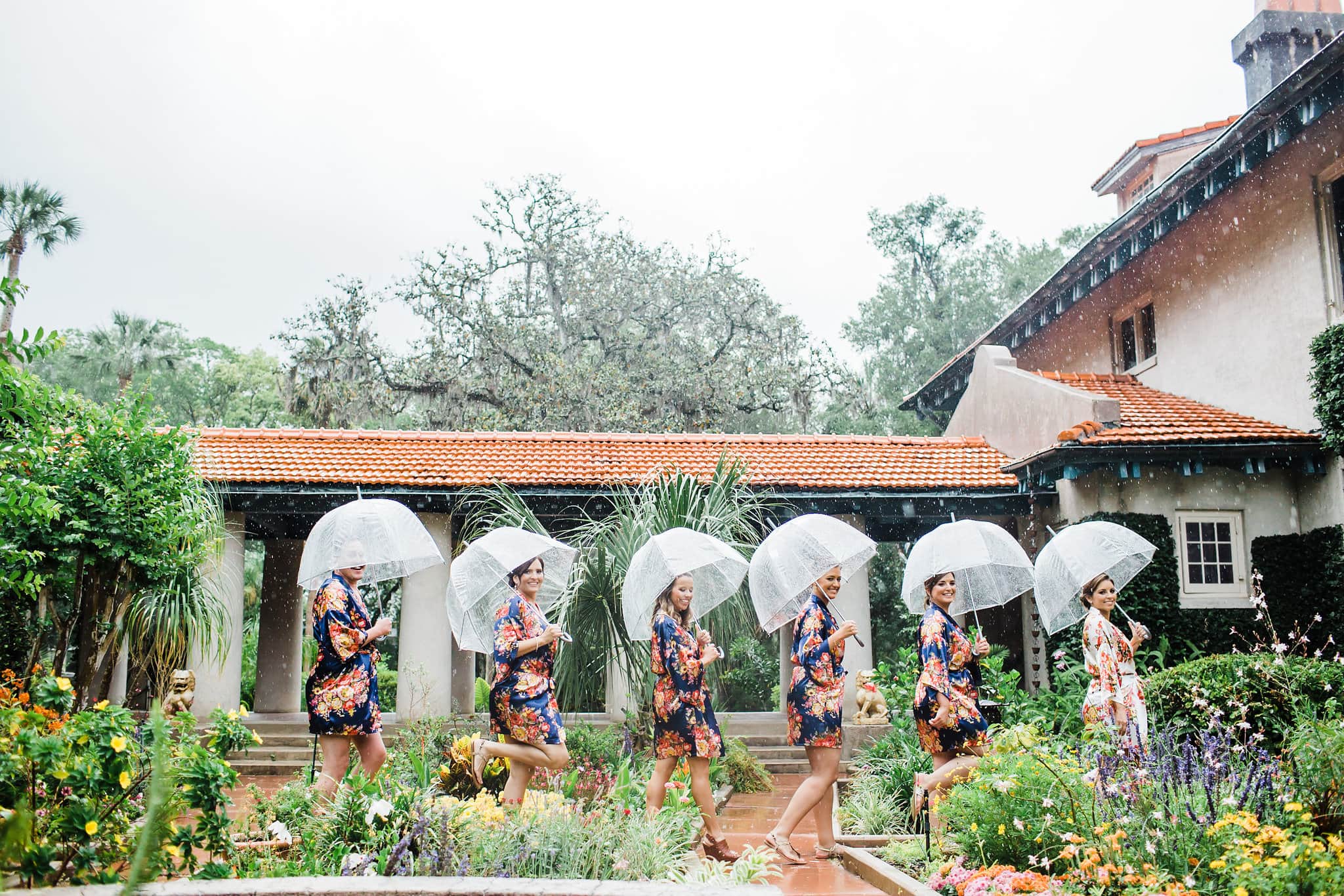 bride and bridesmaids walking with clear umbrellas on rainy Sydonie mansion wedding day