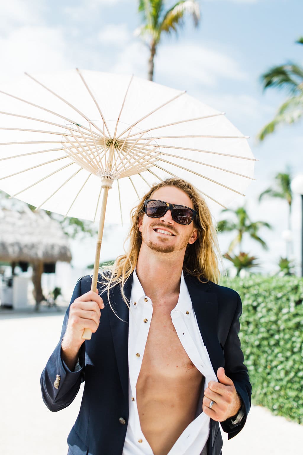 groom with sun umbrella smiling at camera with in florida keys after wedding