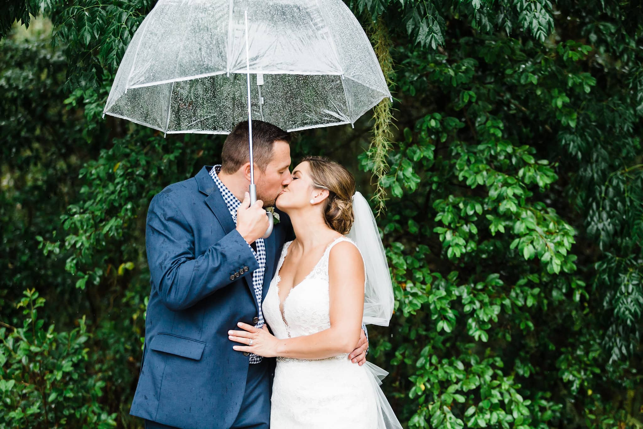 rainy wedding photos with bride and groom kissing under umbrella