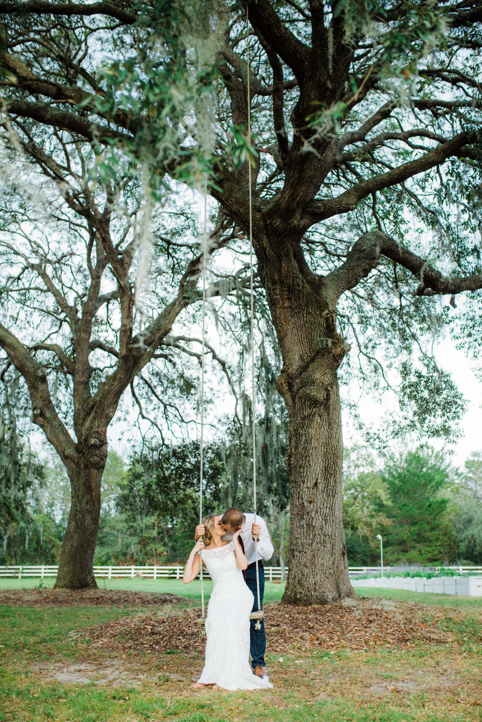 bride and groom kissing on swing underneath large oak trees at bramble tree estate wedding 