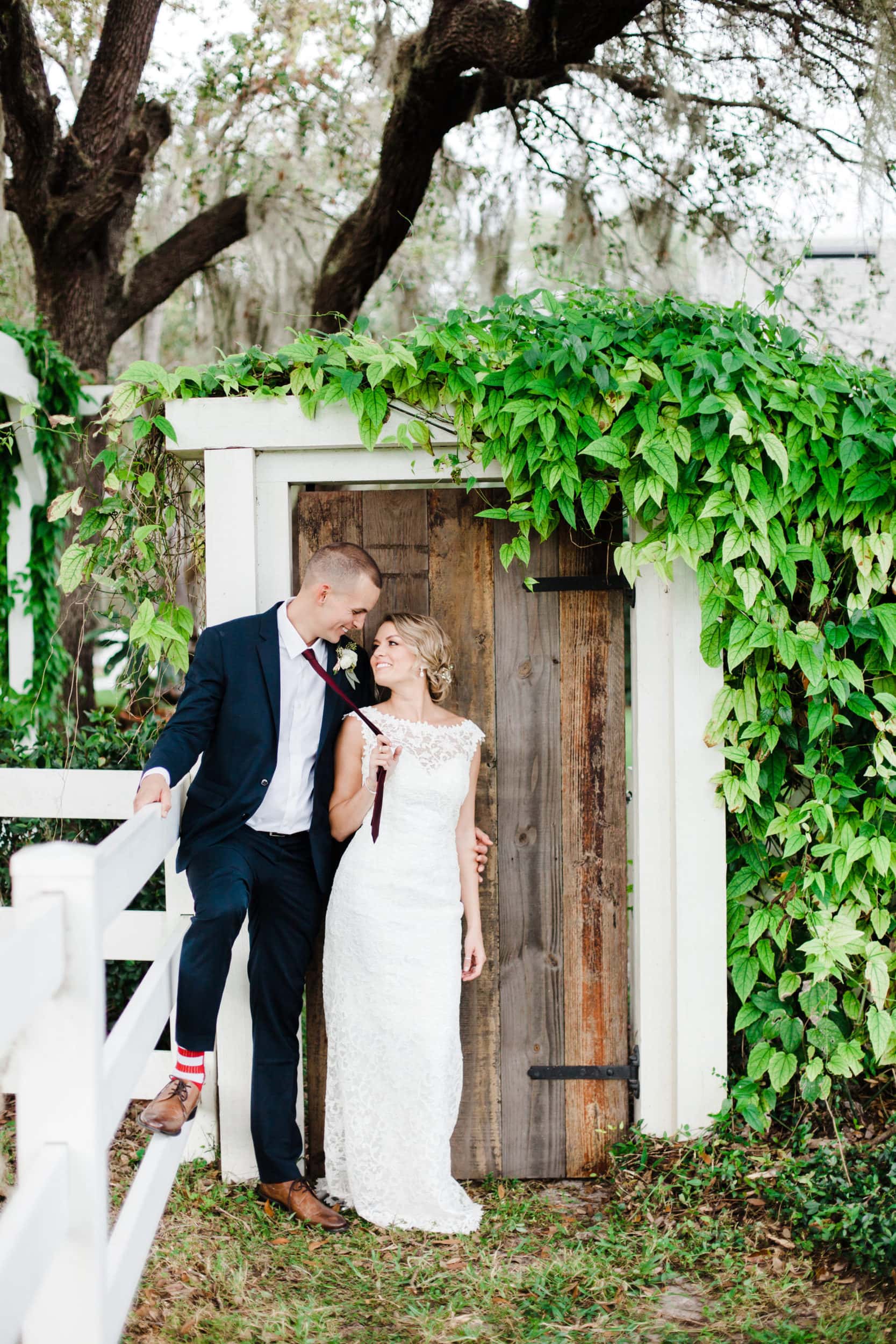 bride pulling room in for a kiss in front of bramble tree estate wooden garden door surrounded by growing live plants