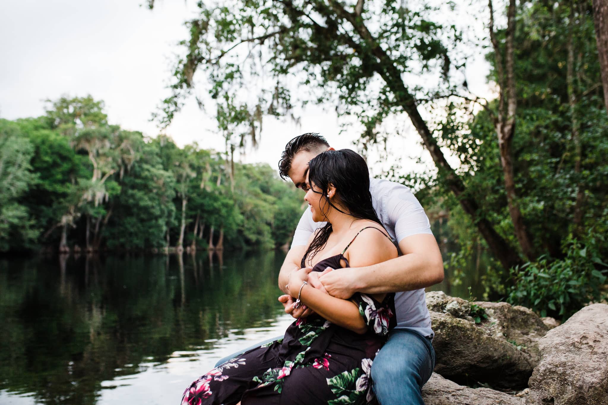 man with arms wrapped around fiancé on the rocks surrounding the ginnie springs river
