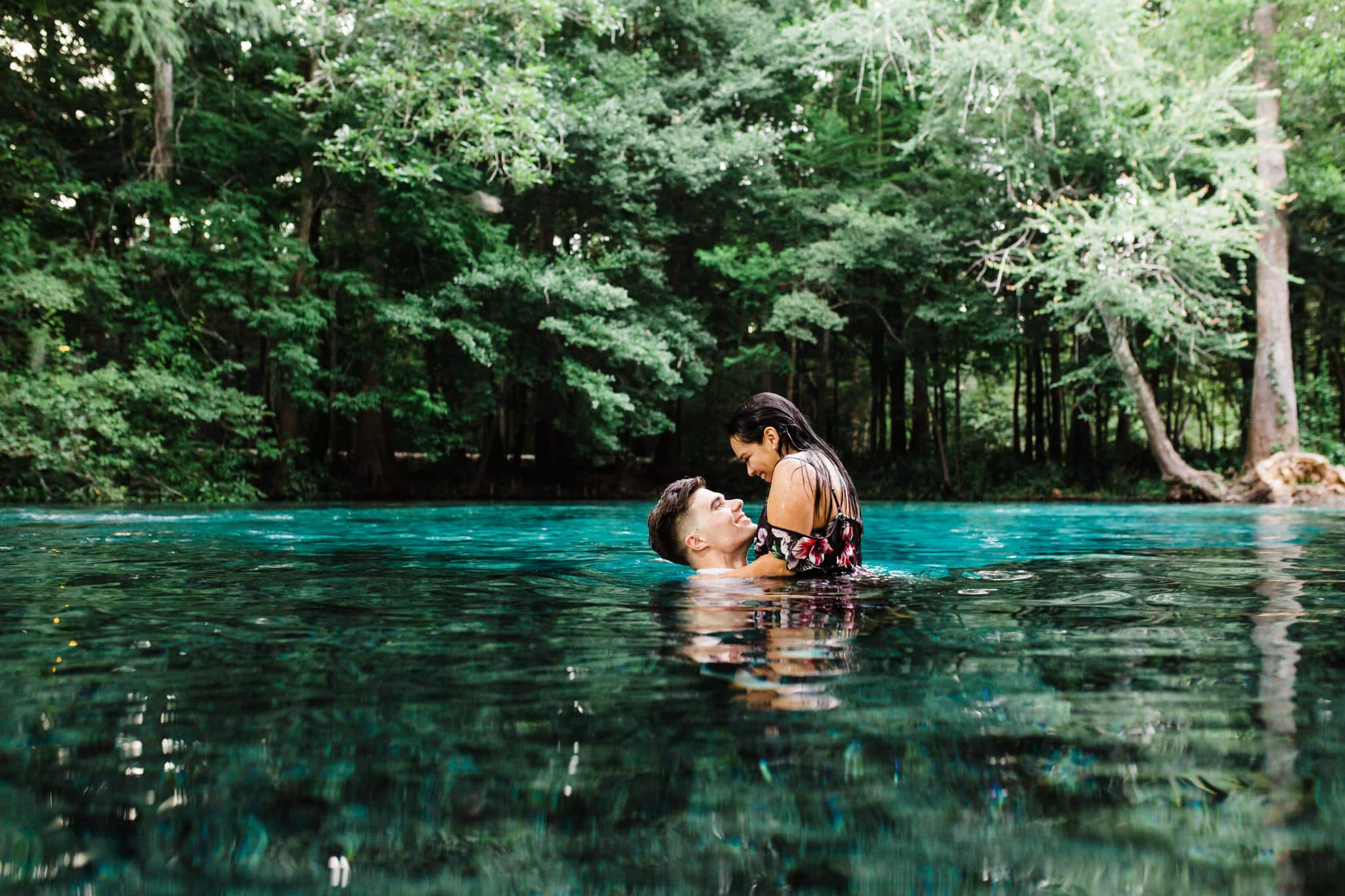 guy holding girl up in the air in the blue water during engagement session at ginnie springs