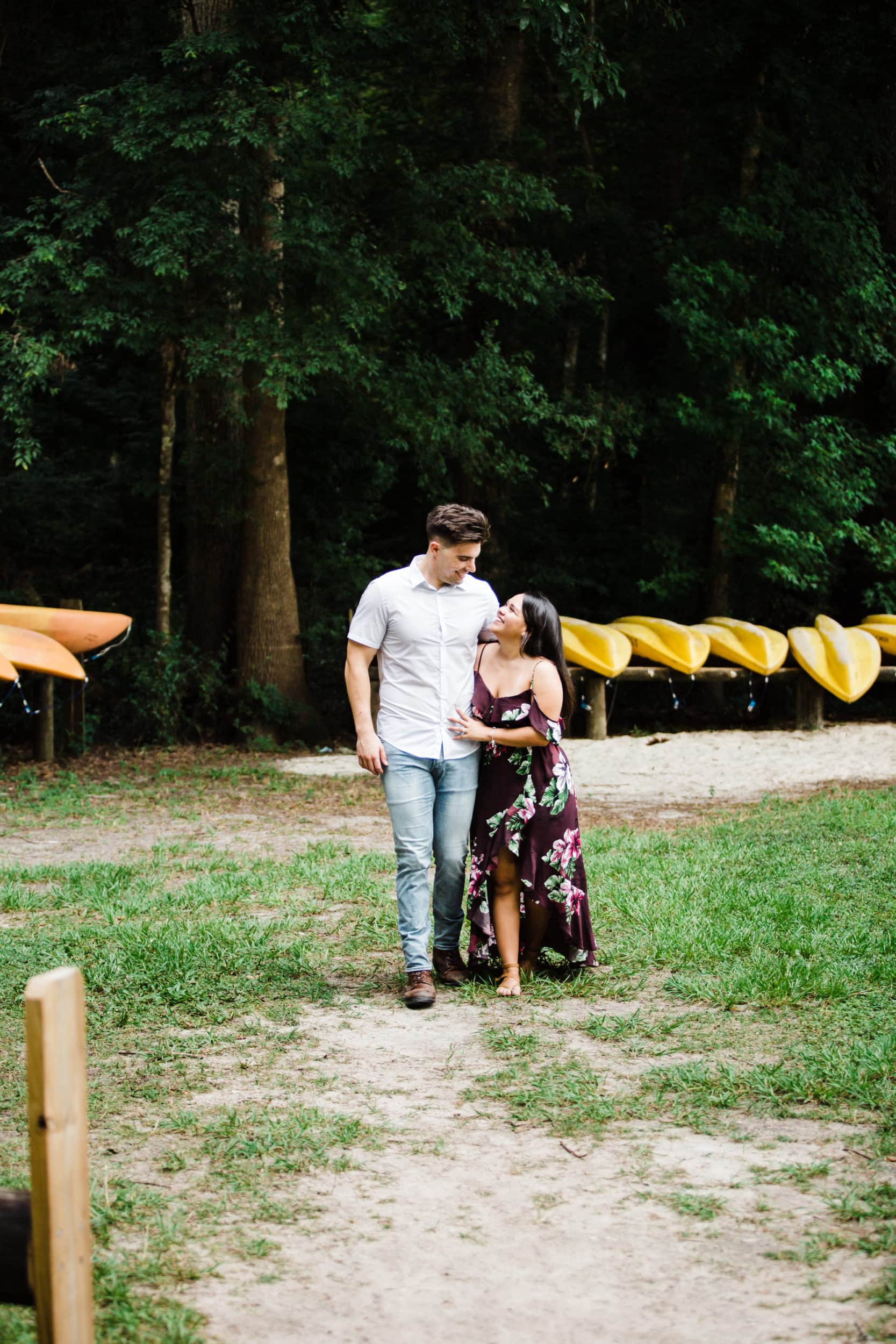 girl in a long dress walking with fiancé in a white shirt and jeans in front of kayaks at ginnie springs