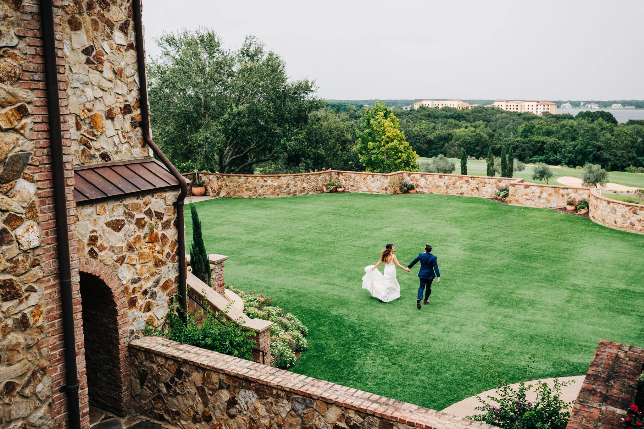 bride and groom running across front lawn at Bella Collina together holding hands with view from above