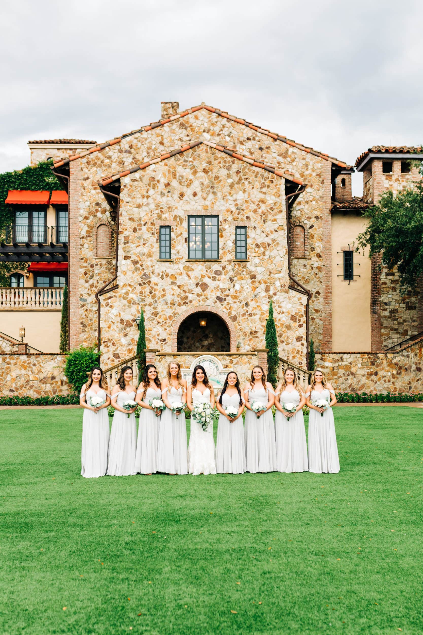 bridesmaids in grey dresses with white and green bouquets on front lawn at Bella collina