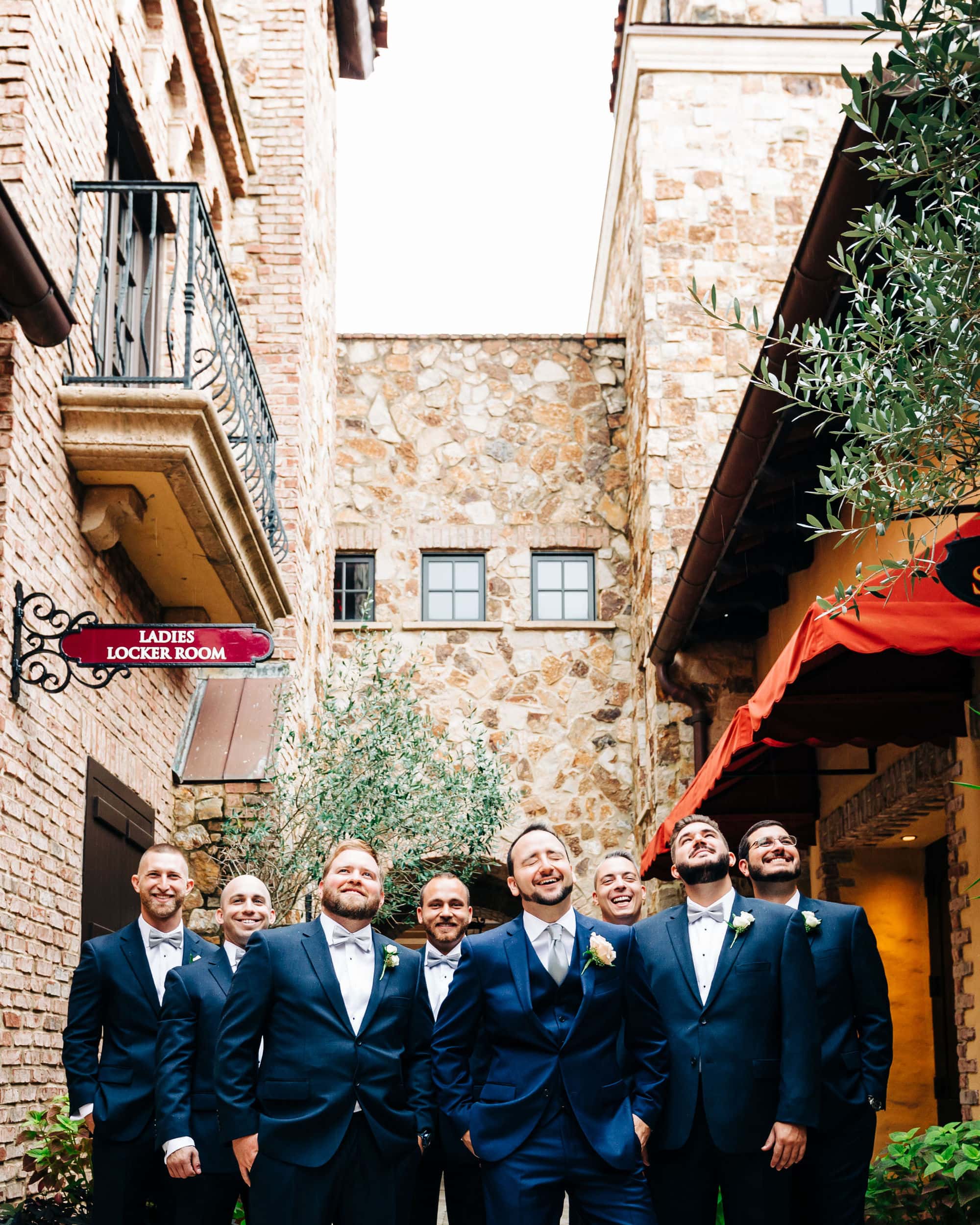 abstract groomsman photo with buildings in the background as the majority of the photo with men at bottom in blue tuxes at Bella collina