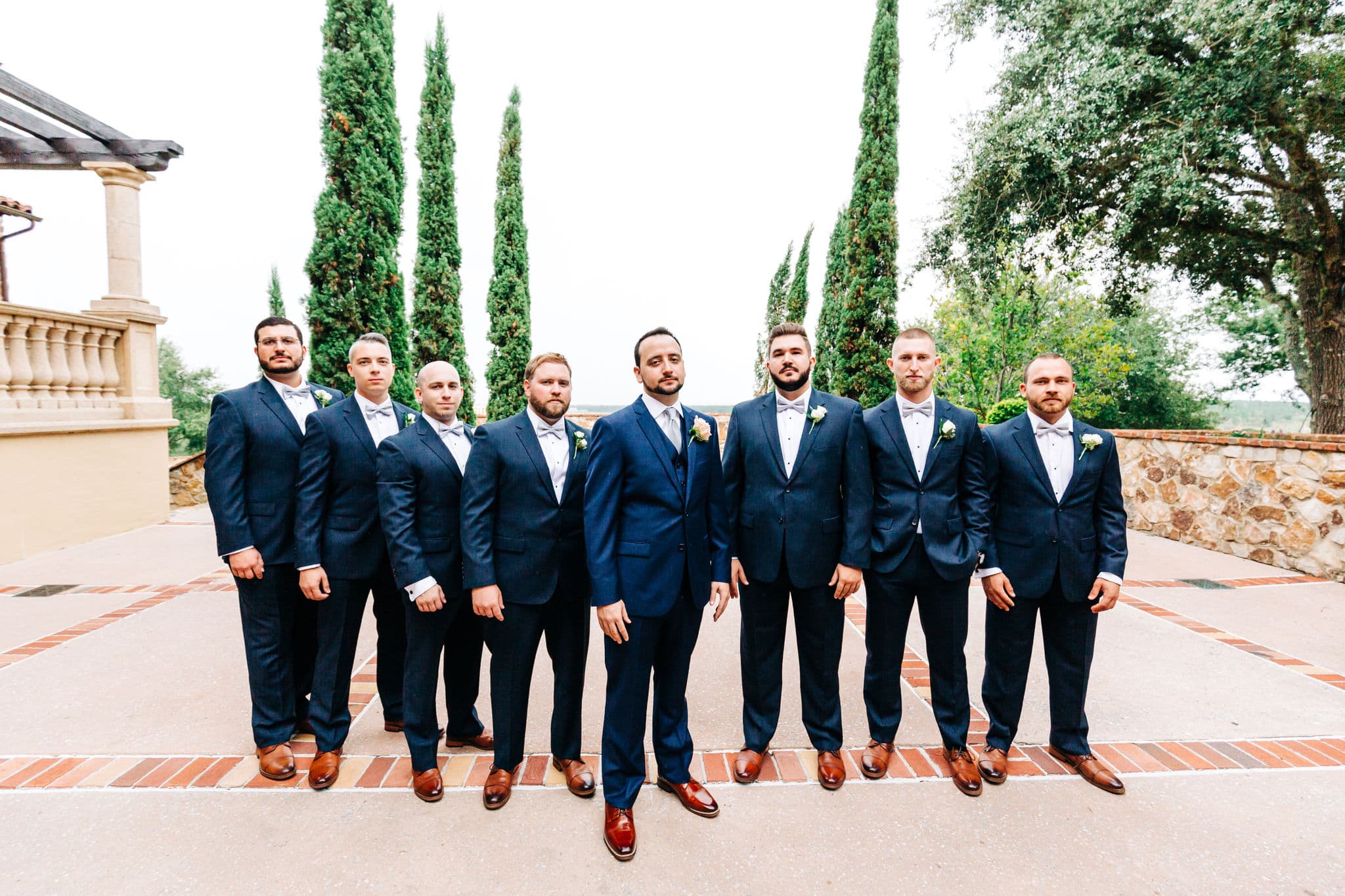 groomsmen in navy tuxes standing together for groomsmen pictures in front of infinity pool at Bella collina