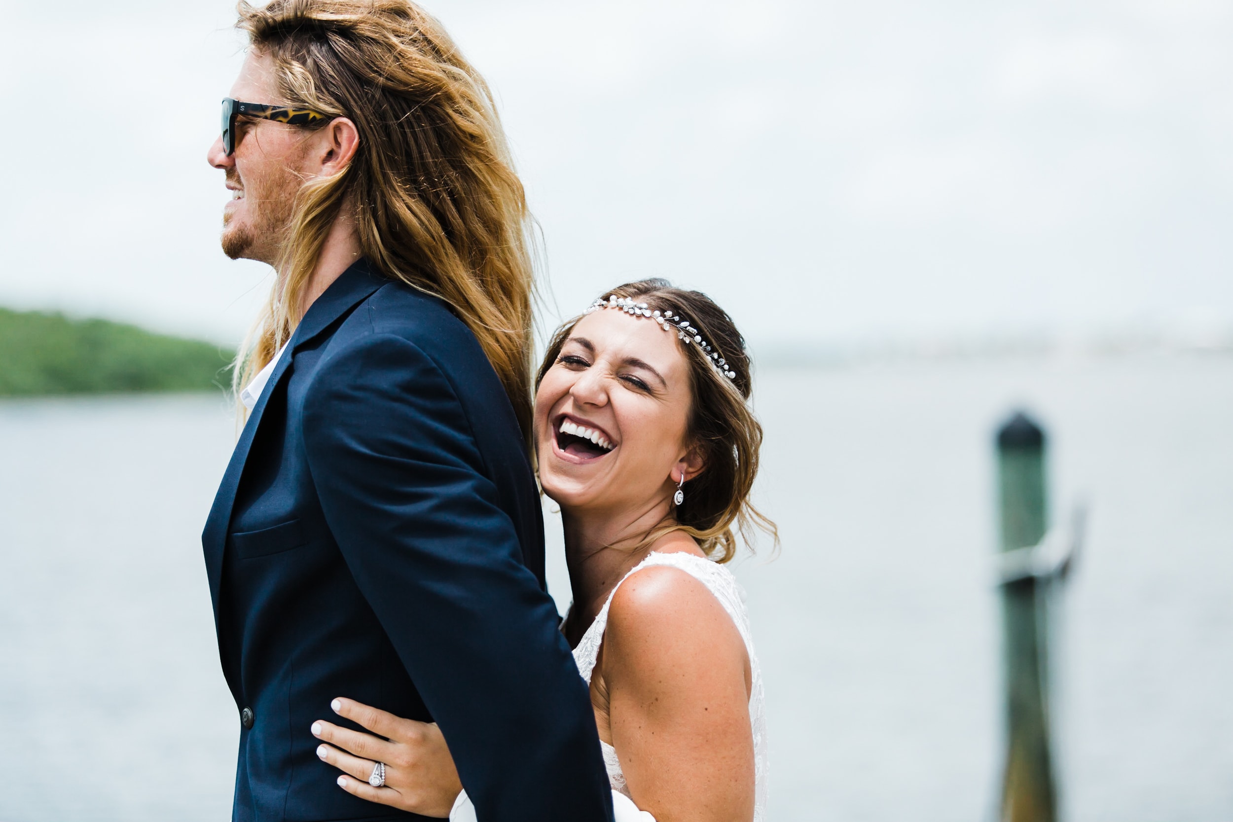 boho bride holding on to groom from behind during first look on the dock of the coconut palm inn and laughing