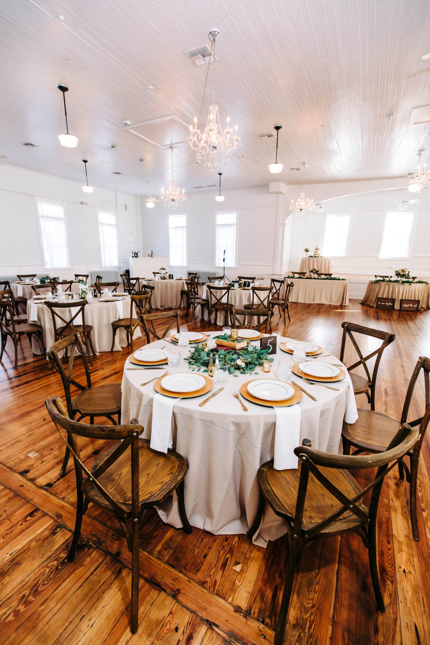 indoor reception with white walls and gold, white, and green table decor with light greenery and wooden tables