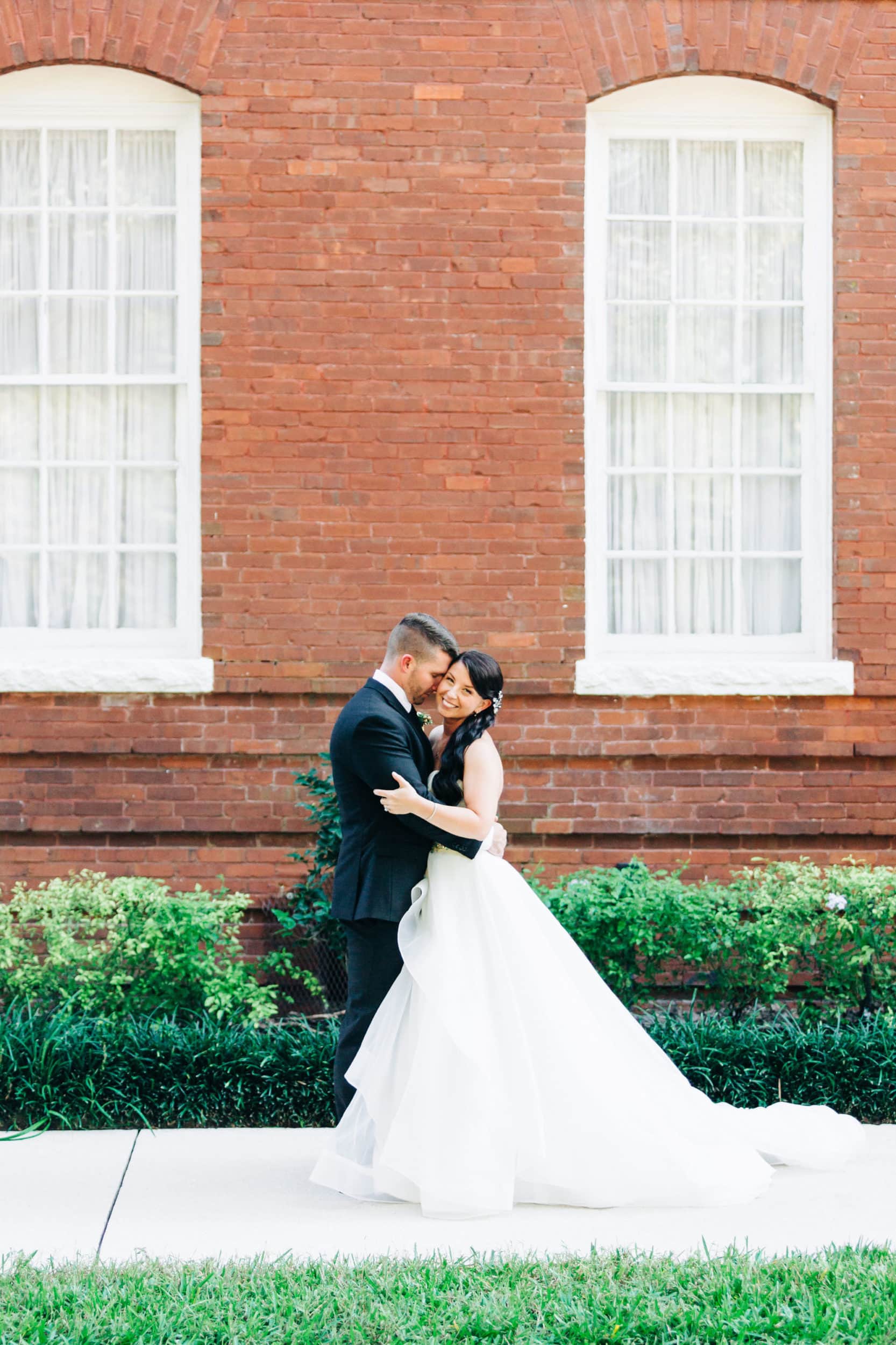 groom holding bride intimately between white windows in front of red brick walls