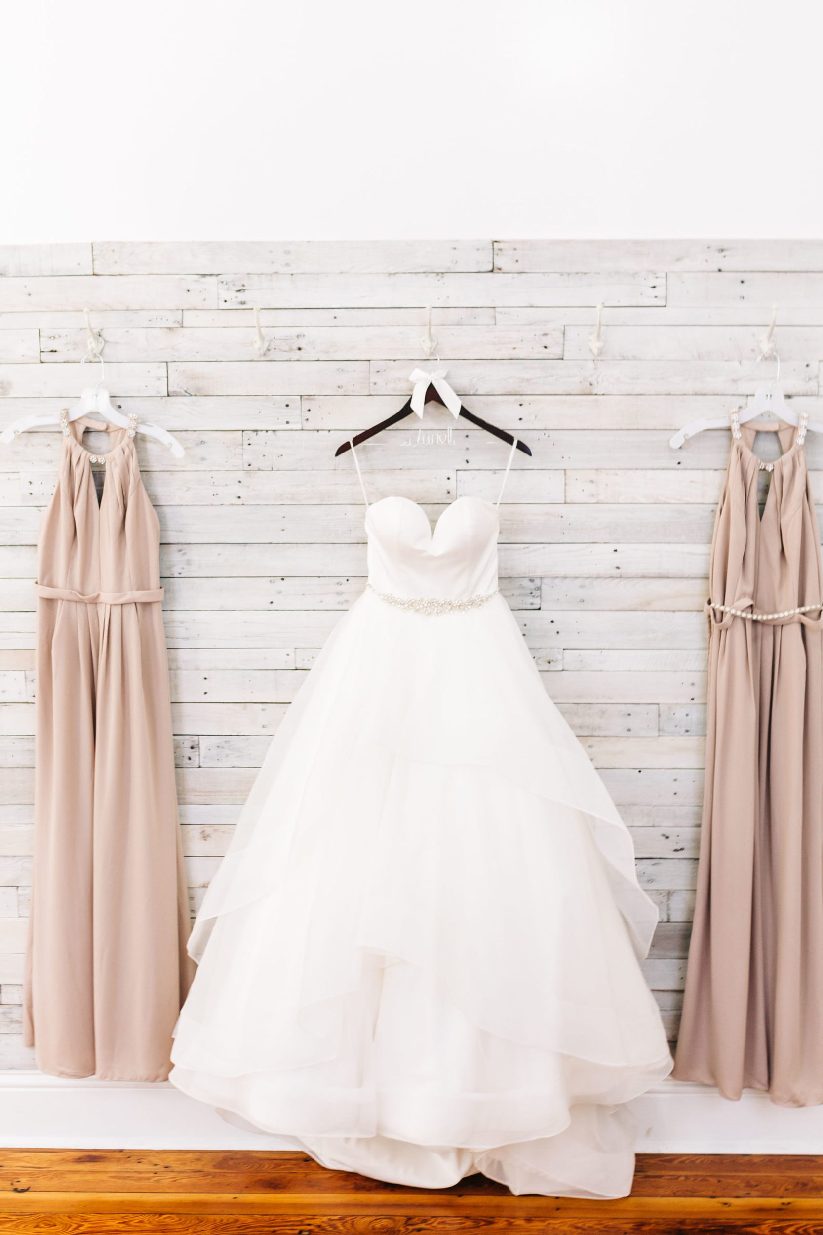 bridal gown hanging in bridal suite at venue 1902 with bridesmaid dresses hanging next to the gown