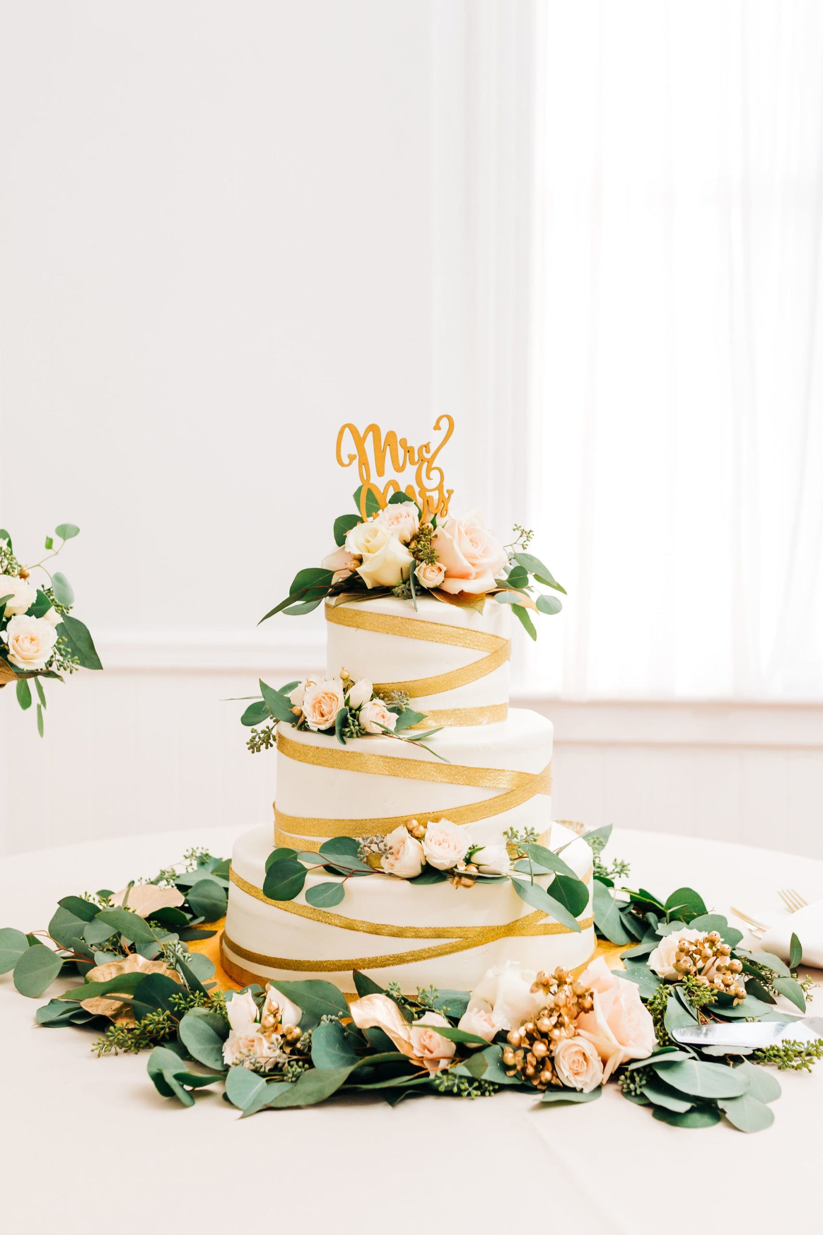 simple gold and white wedding cake with greenery and roses