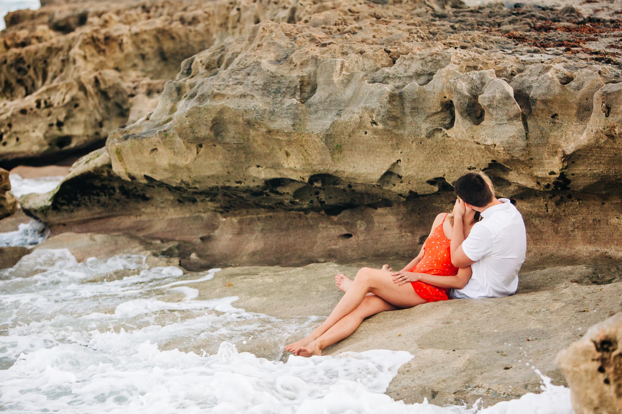 couple kissing under the rocks with waves crashing in at blowing rocks preserve