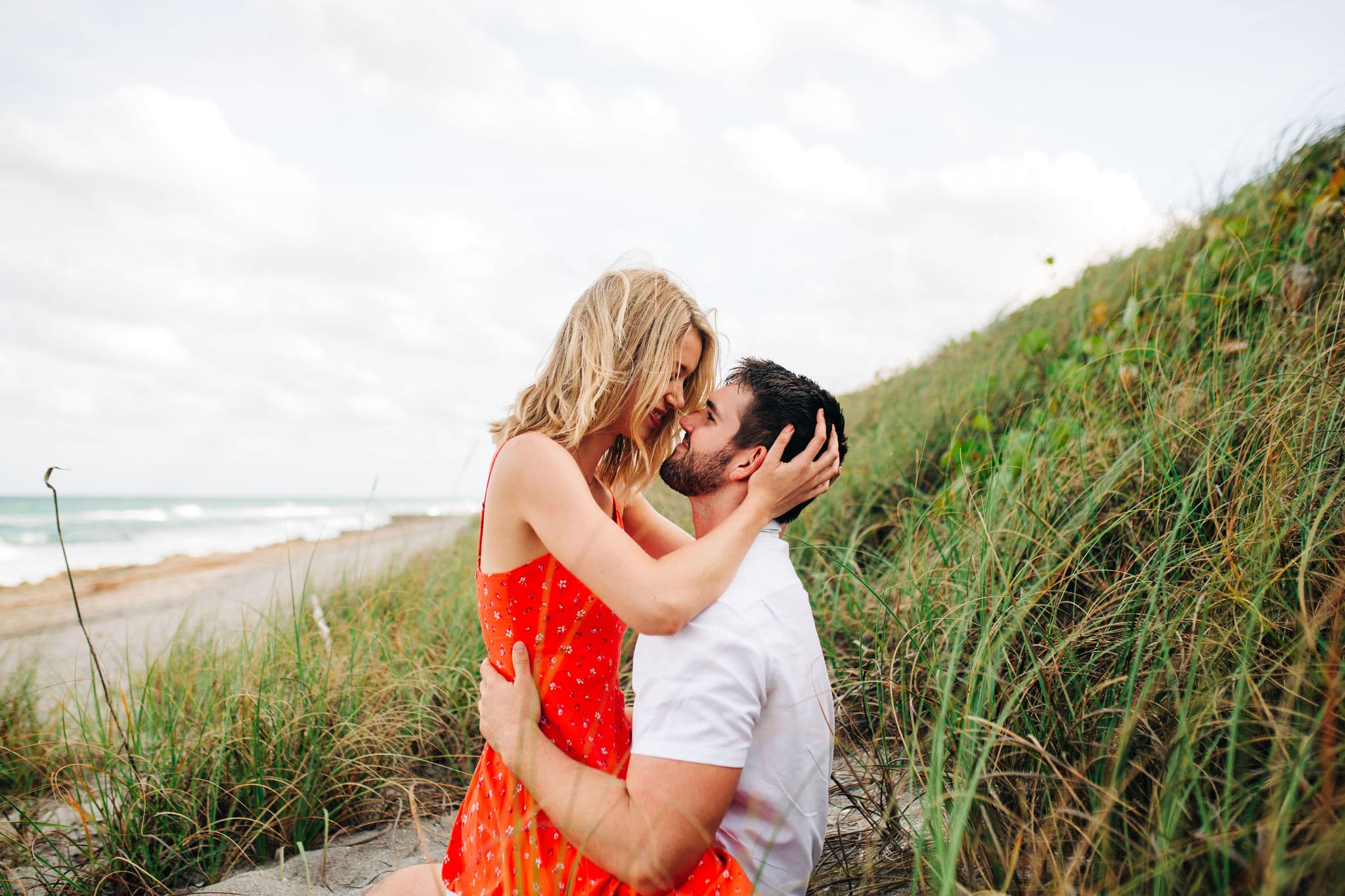 couple kissing in the tall grasses that are on the sand mound on the edge of blowing rocks preserve