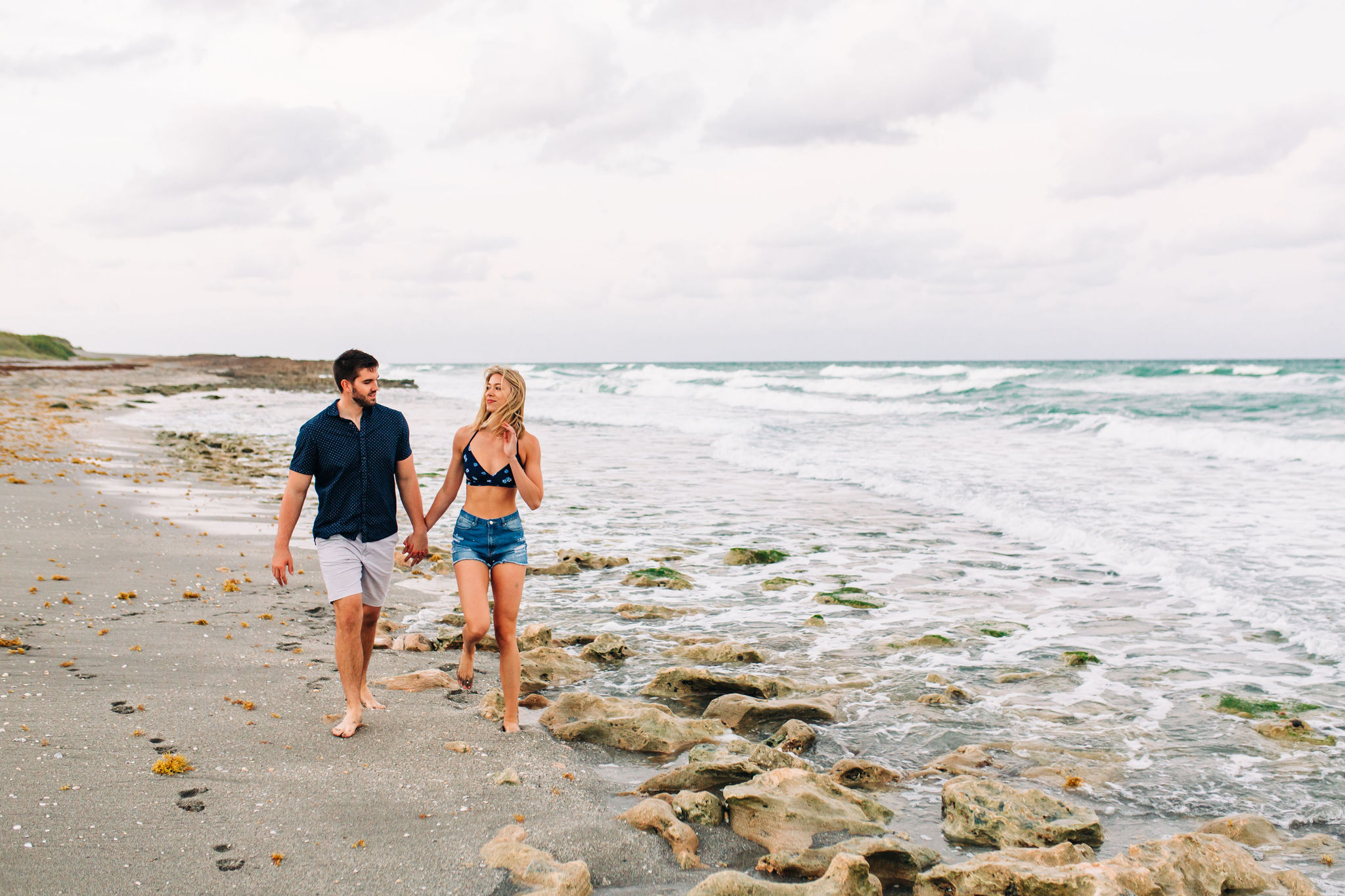 couple walking along the beach shore during engagement session at blowing rocks preserve