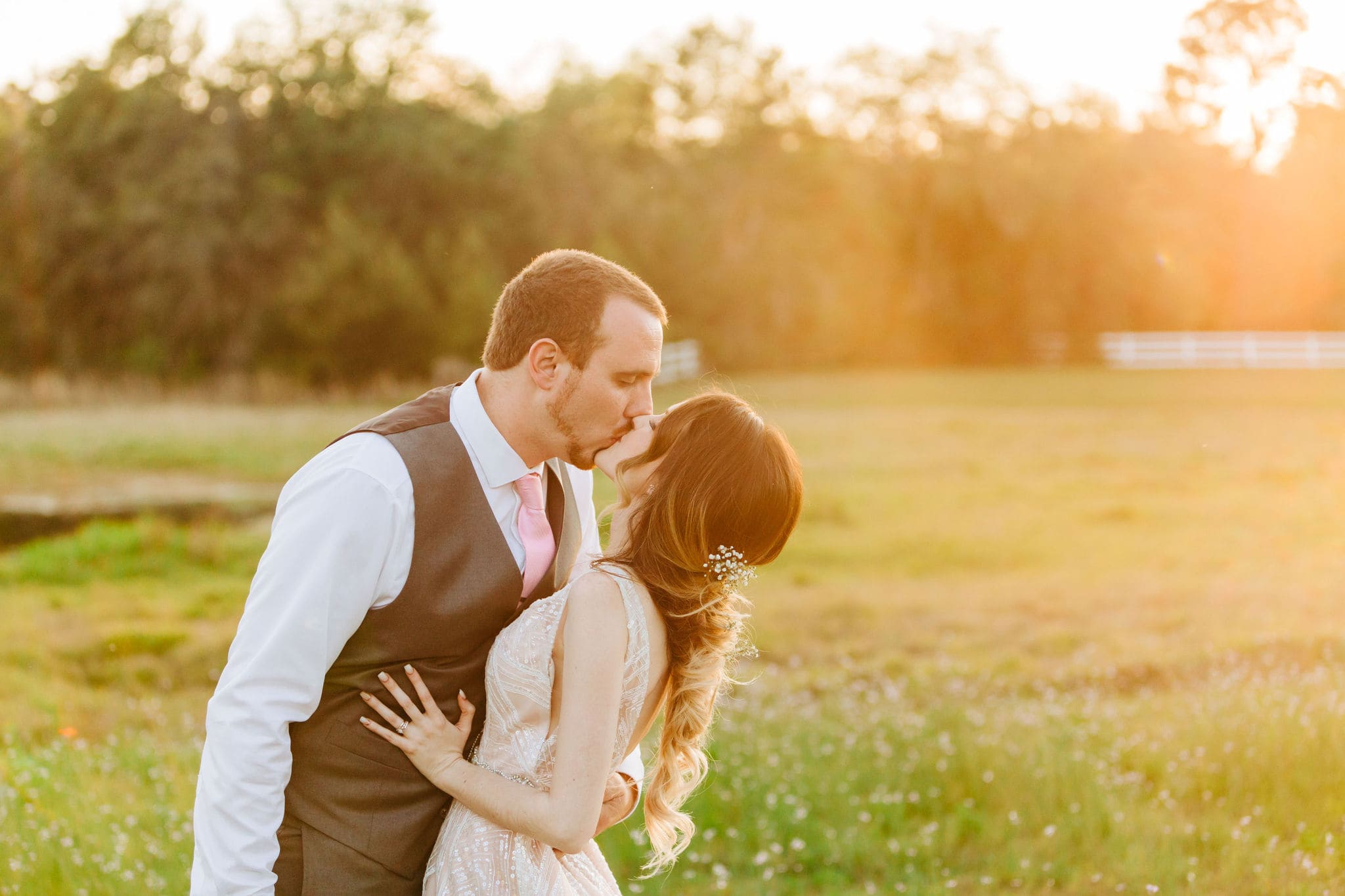 bride and groom kissing on field at bramble tree estate with sunset flare in background