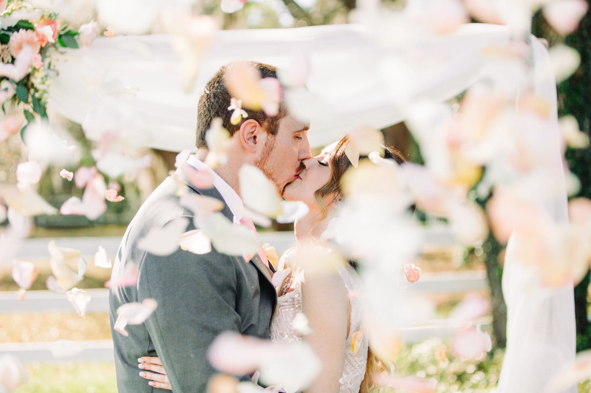 bride and groom kissing with rose petals falling in the air around them
