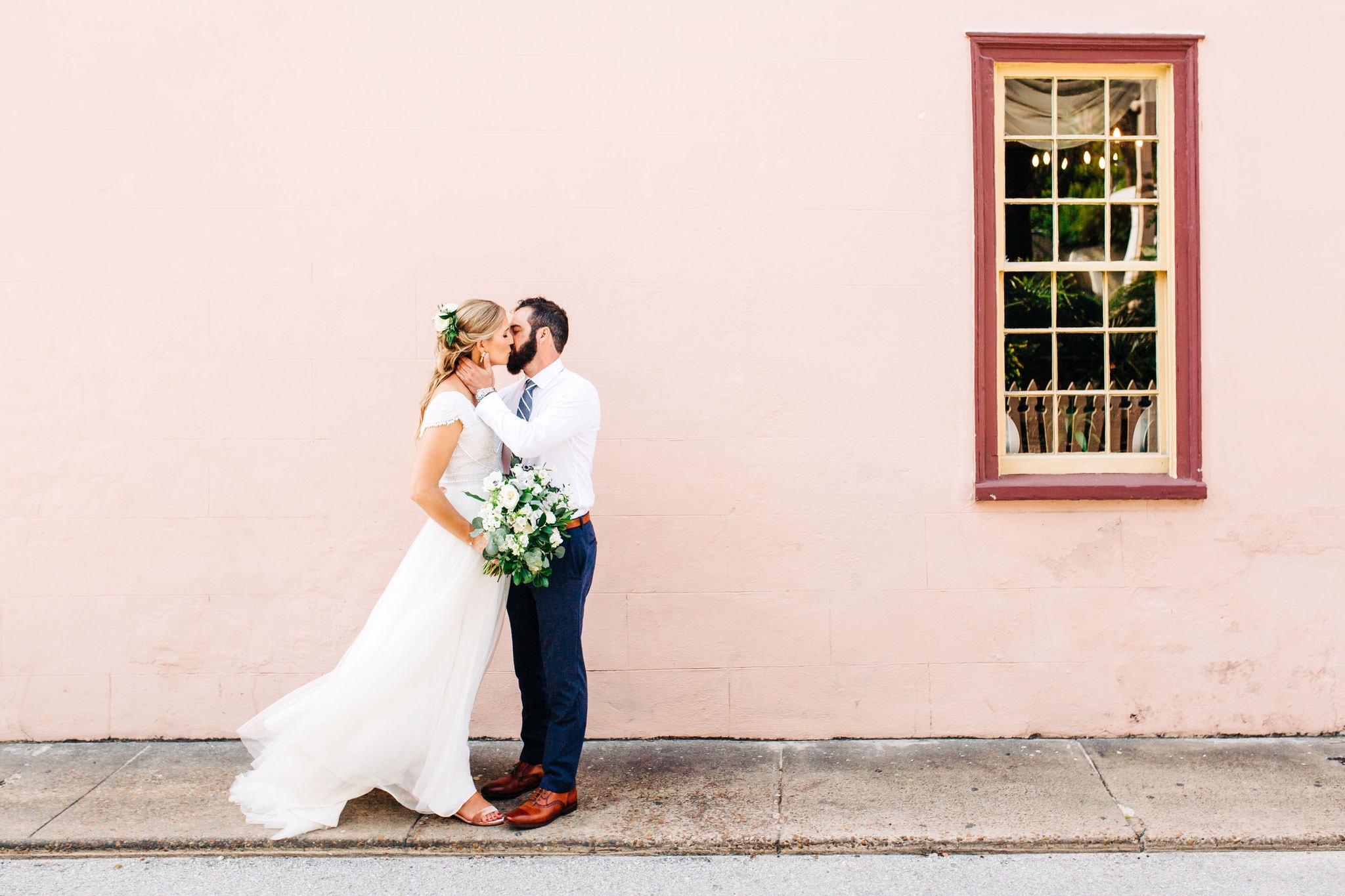 bride in white gown with groom with pink building background at white room wedding