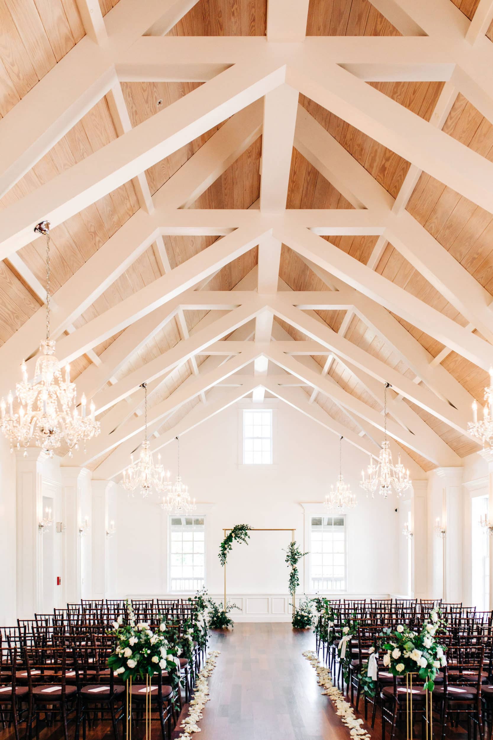 wooden pews with white cathedral ceiling with gold archway with greenery and white flower garland at white room wedding
