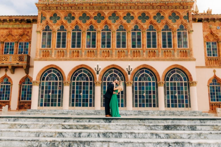 girl in green dress being kissed by groom in blue suit in front of the ringling museum