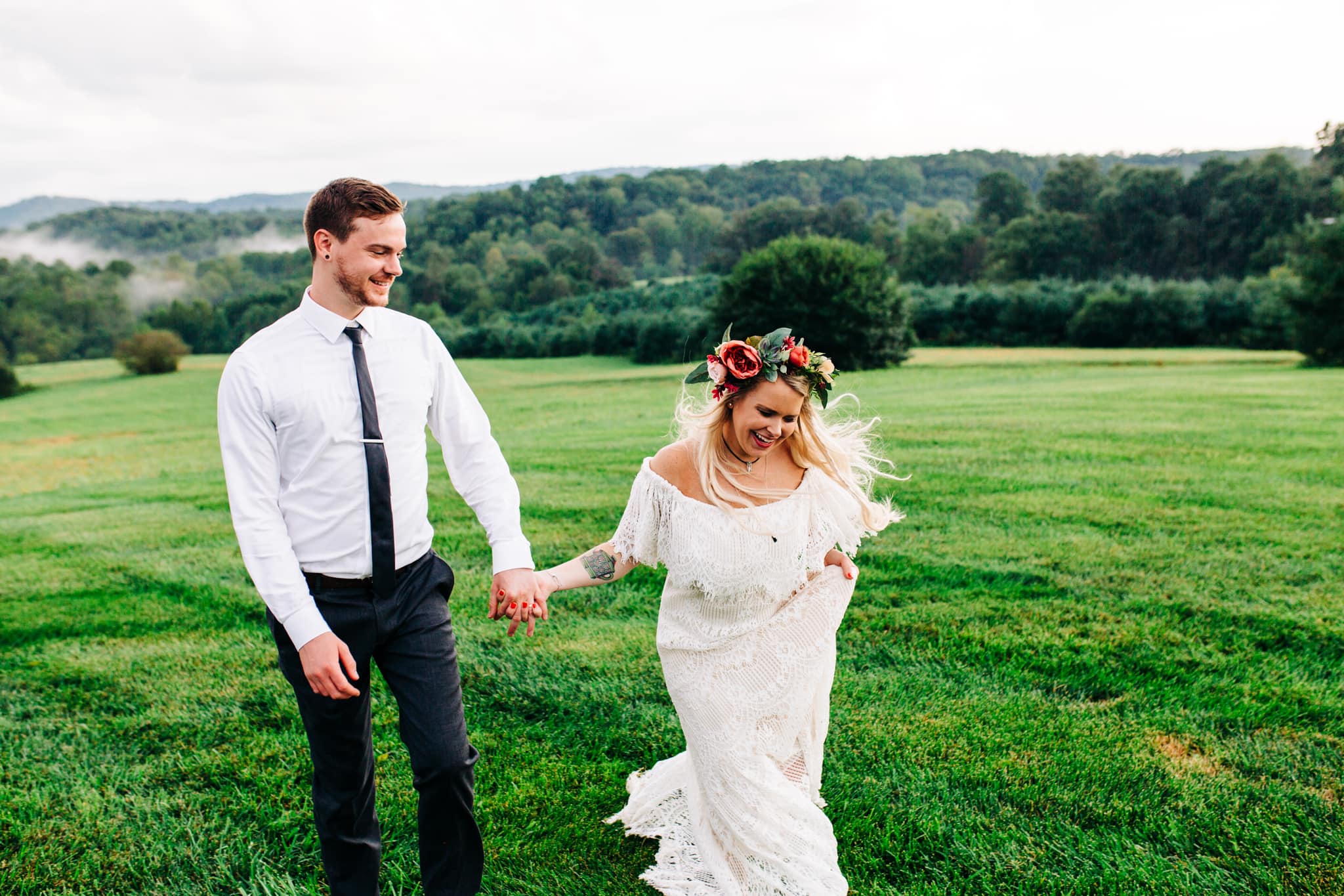 boho bride with flower crown laughing and walking with groom while holding hands along the lawn of gambill estate wedding venue in roaring river North Carolina