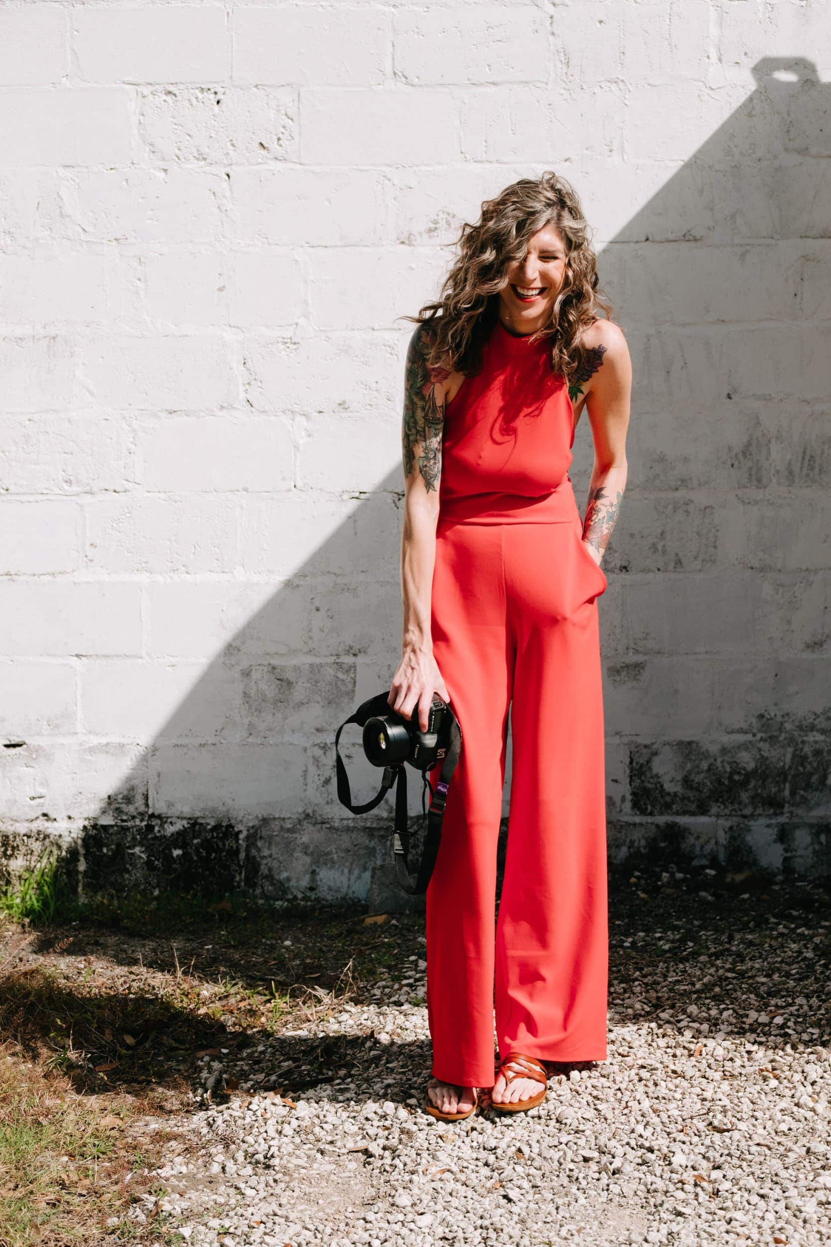 Photographer in red jumpsuit laughing with camera in hand