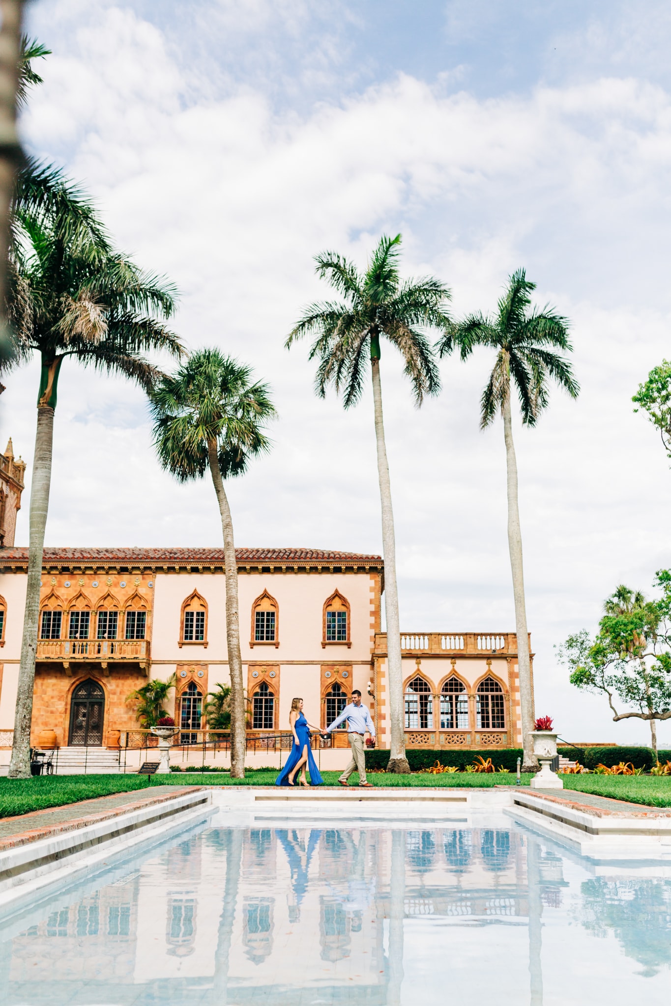 man leading woman along the infinity pool at ringling museum with palm trees and pink building in background