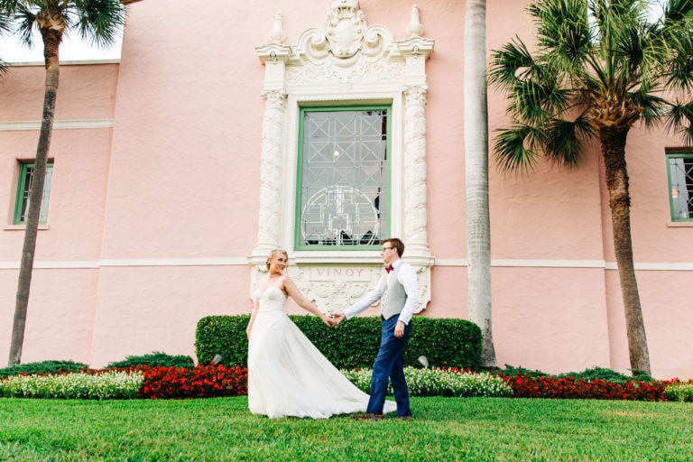 bride in white dress and groom with navy suit with large detailed window and pink building in background at vinoy wedding