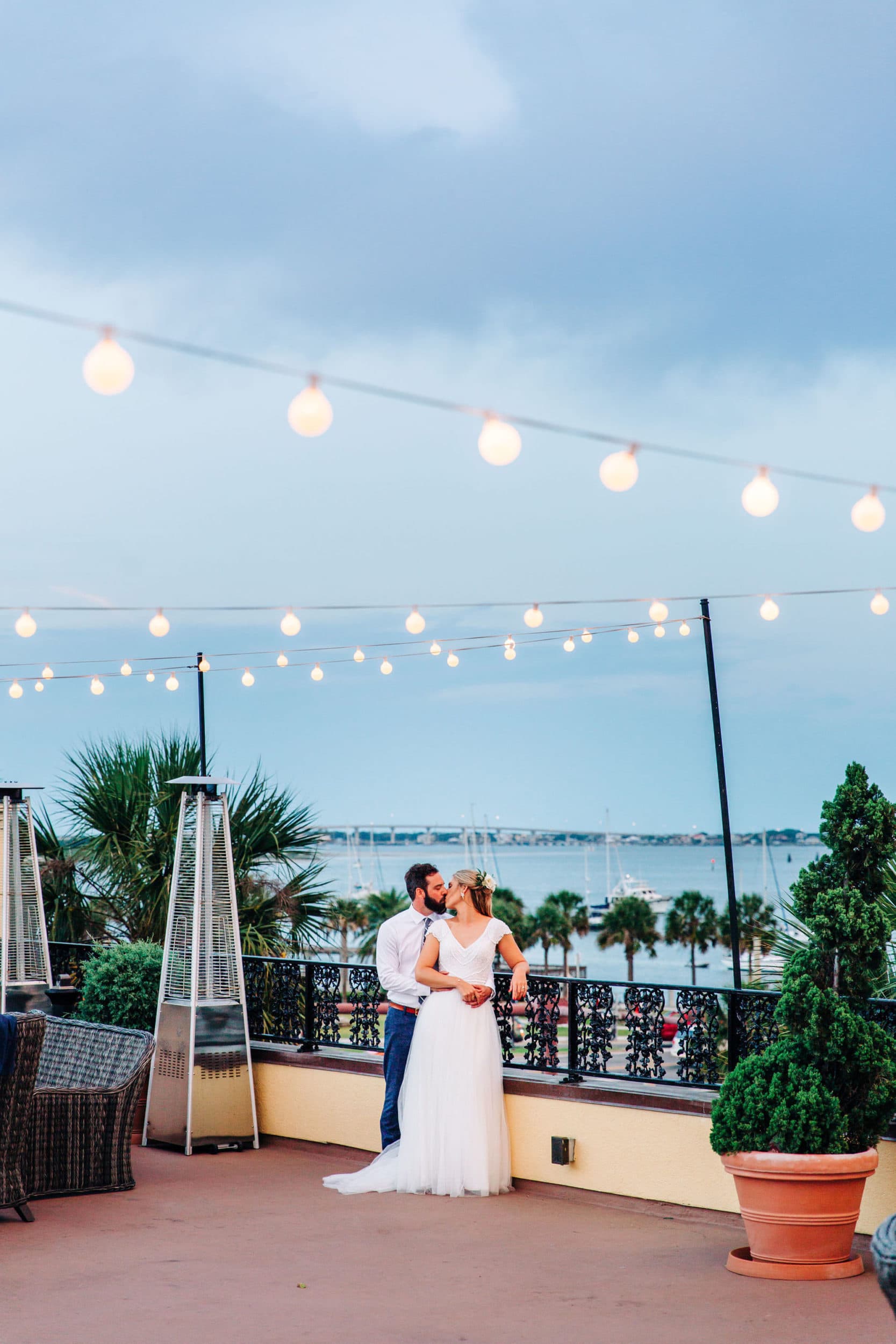 bride and groom with rooftop view with string lights with bay view at white room wedding