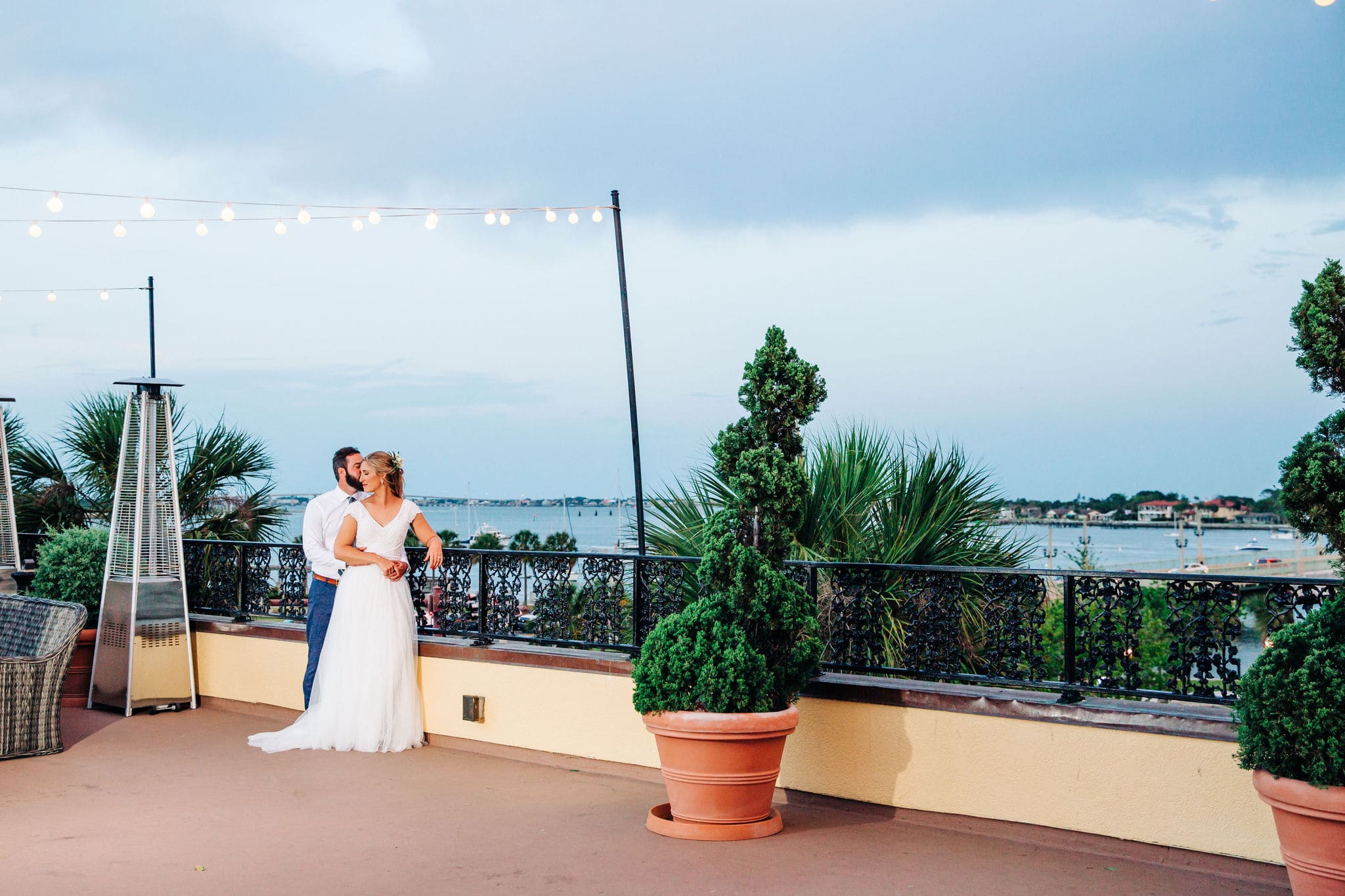 bride and groom with greenery with string lights with rooftop with bay and marina view at white room wedding