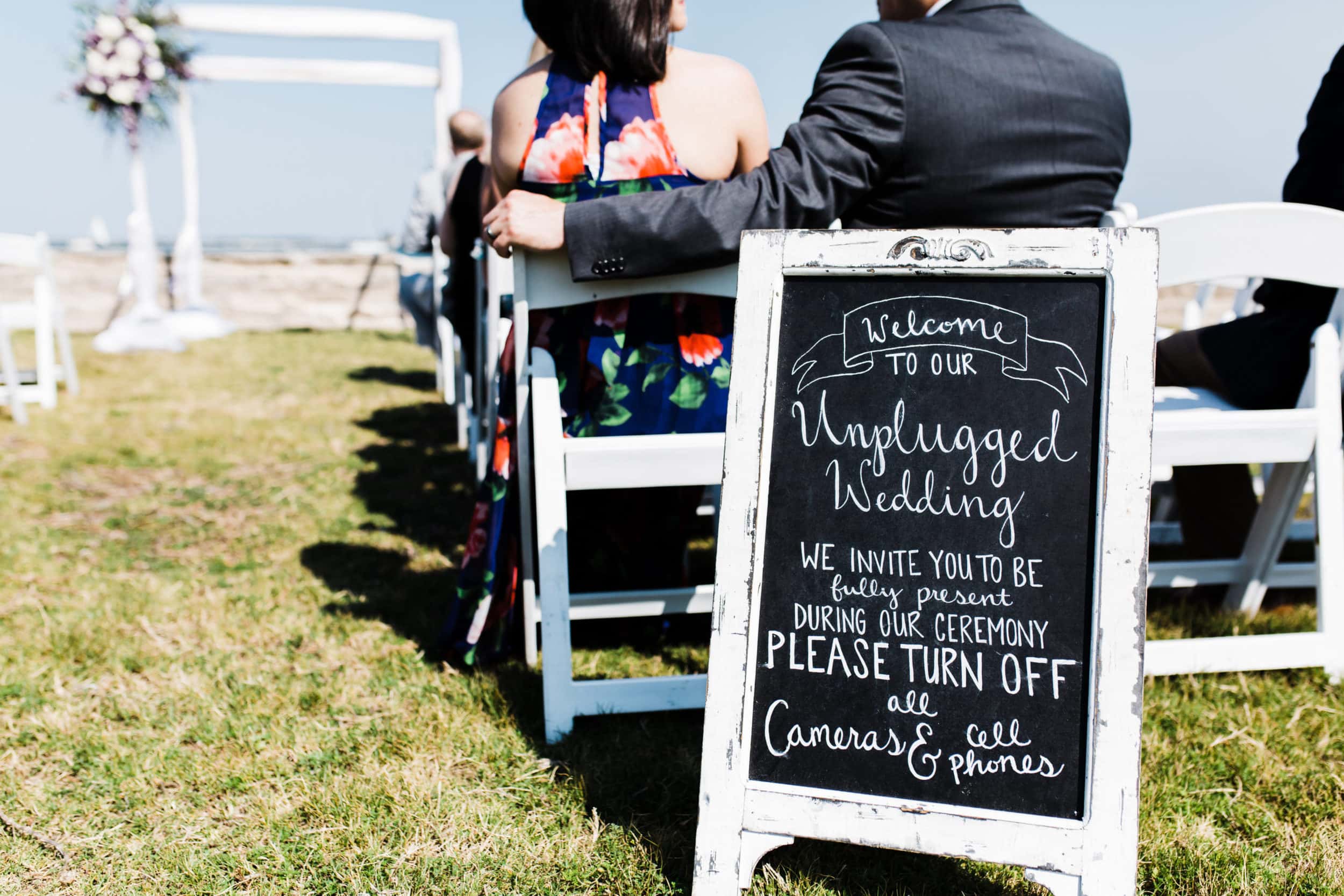 ceremony aisle with welcome unplug chalkboard sign with white chairs at castillo de san marcos wedding