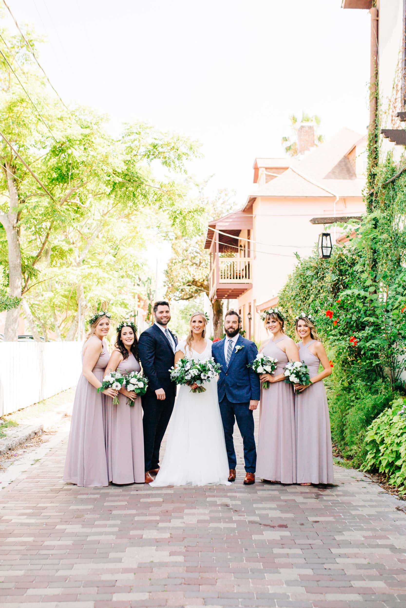 bride and groom with bridesmaids in pale lavender with white flowers and groomsmen with navy suit at white room wedding