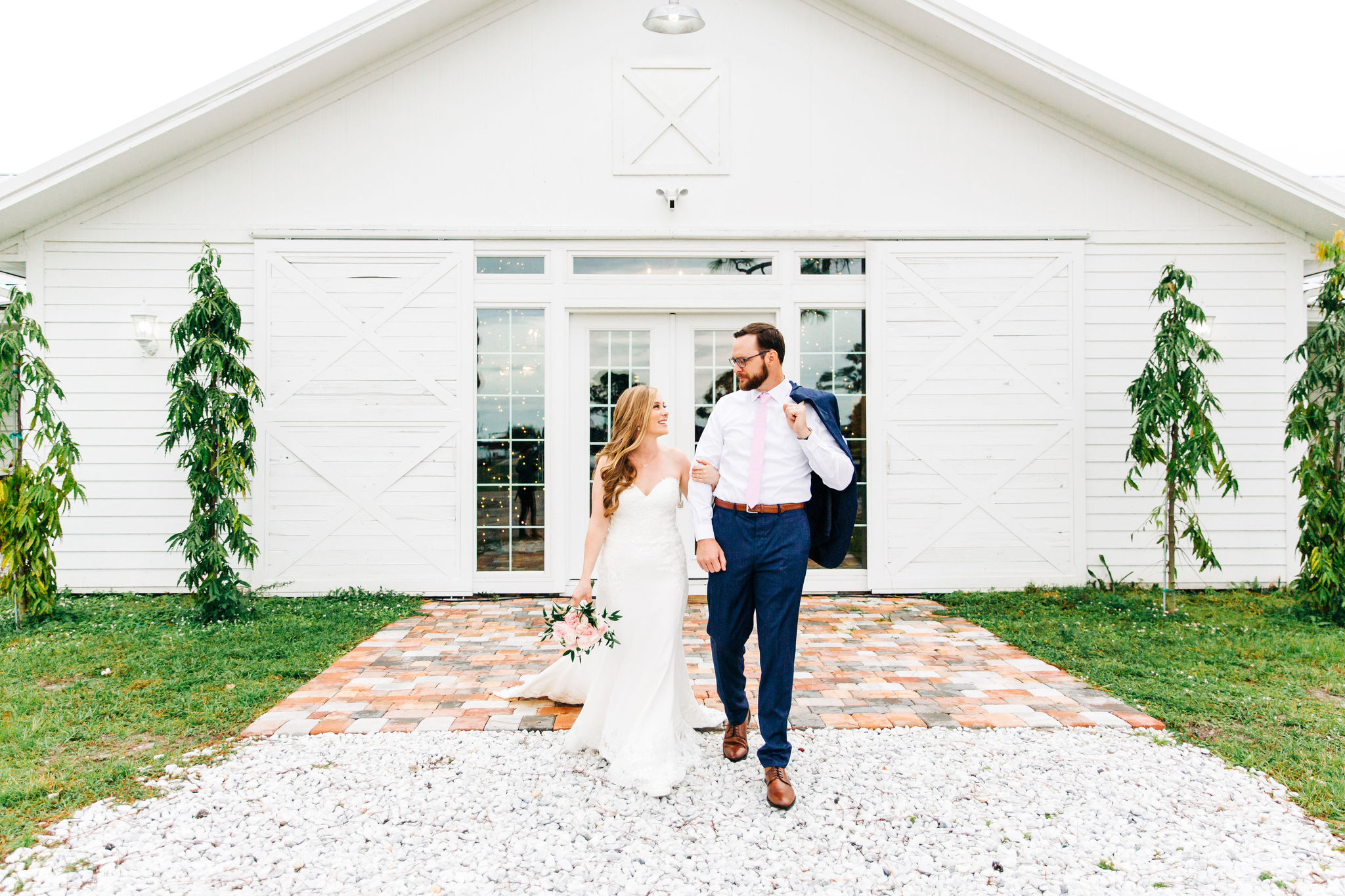 bride and groom in white dress and navy tuxedo in front of white ranch style building with glass french doors at ever after farms ranch