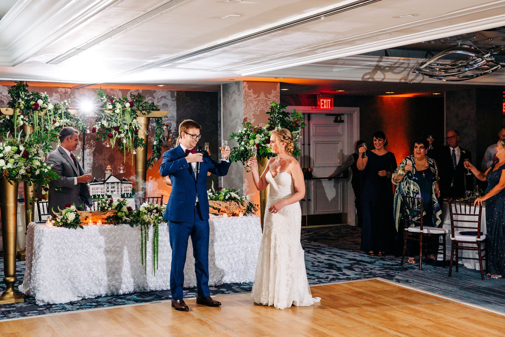 bride with strapless lace dress with groom with navy suit with wooden dance floor with bridal tablescape in background at vinoy wedding