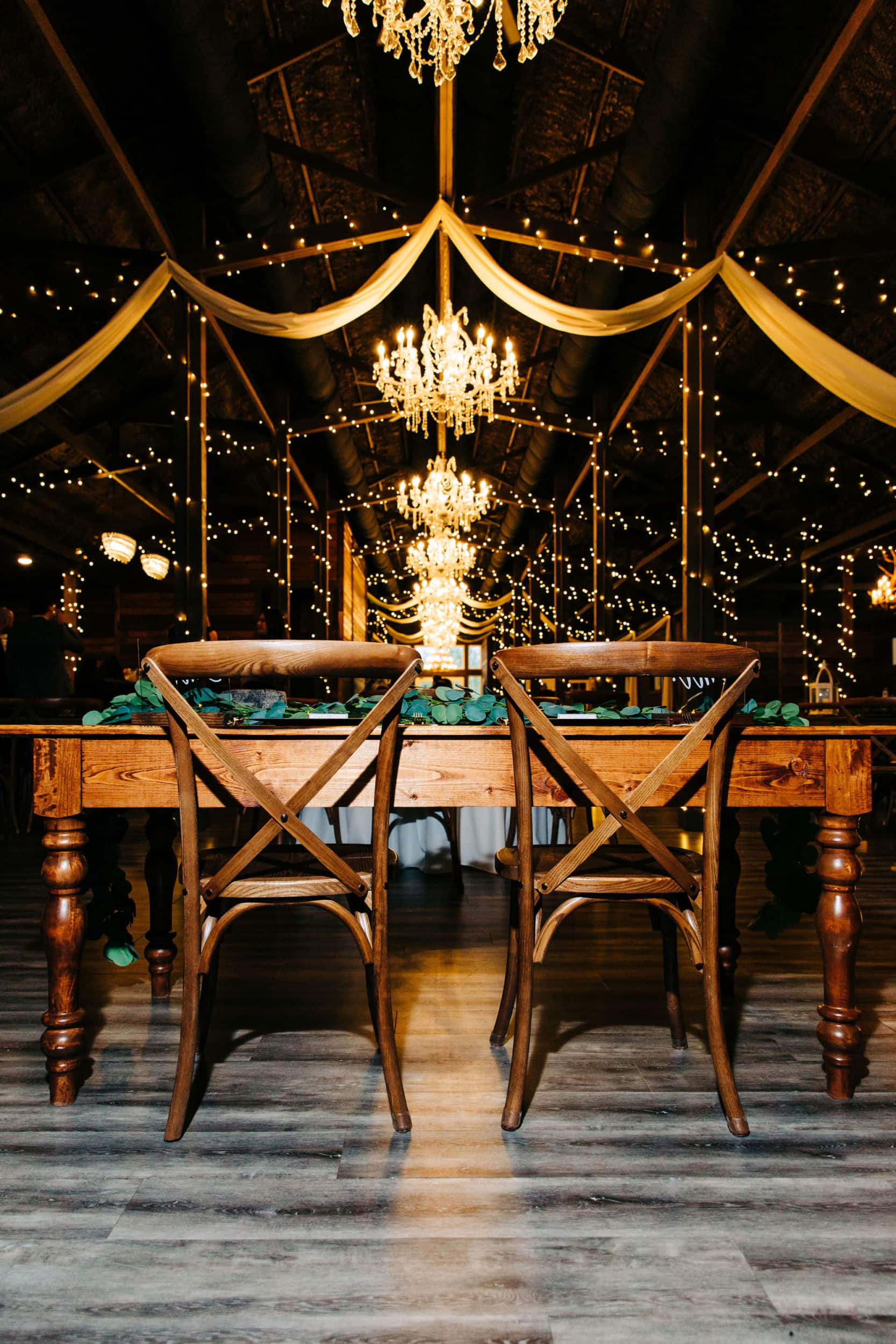 wooden chairs and table inside of wooden interior with chandeliers and garland lights