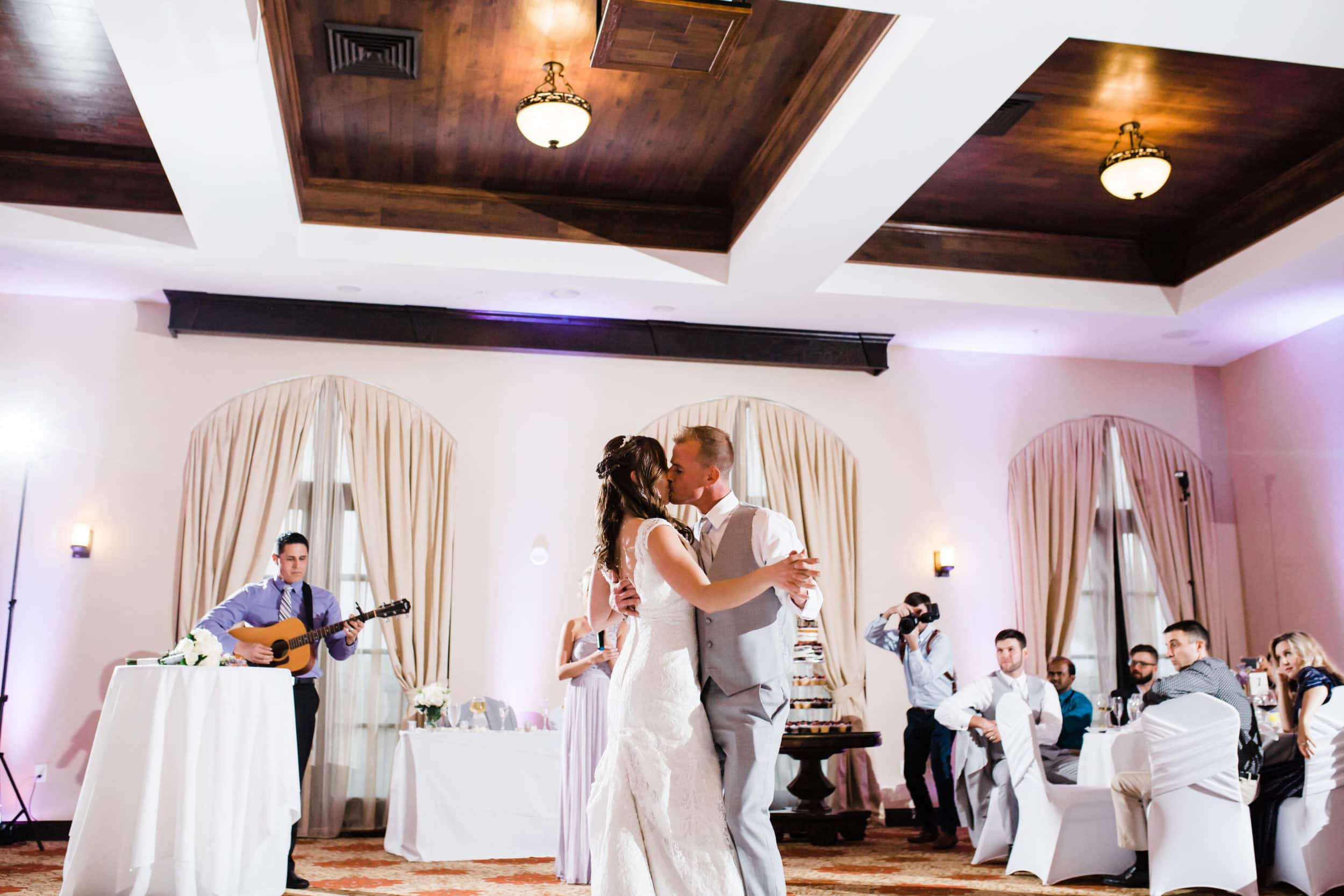 bride with white dress and groom with grey suit first dance with guitarist singing with white and wood interior with guests cheering at castillo de san marcos wedding