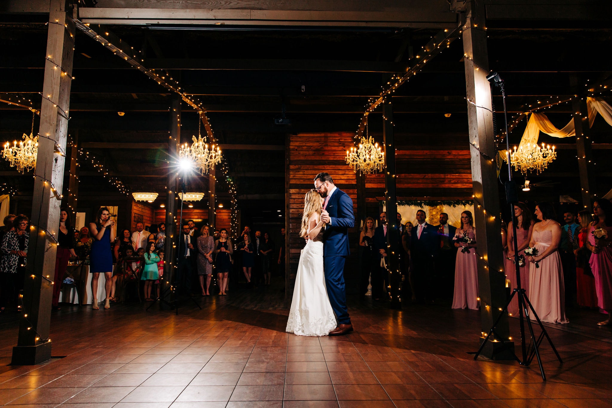 bride in white gown and groom in navy tuxedo sharing their first dance in reception area with wooden interior at ever after farms ranch