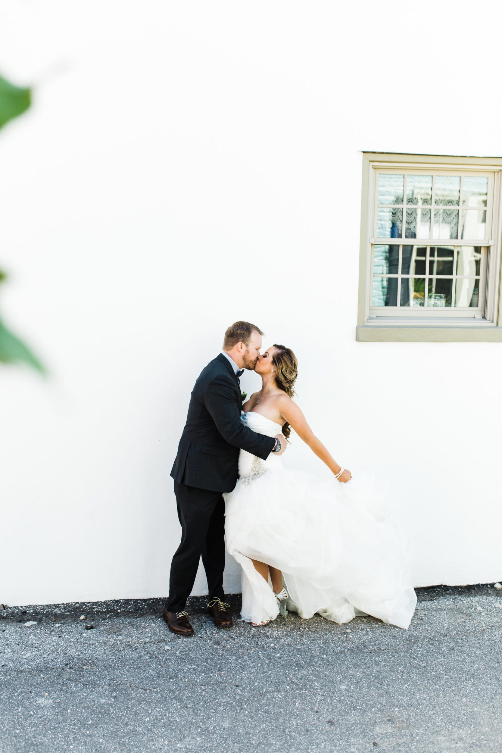 bride with sleeveless dress with groom with black suit with white building in background at Saint Augustine Sailboat Elopement